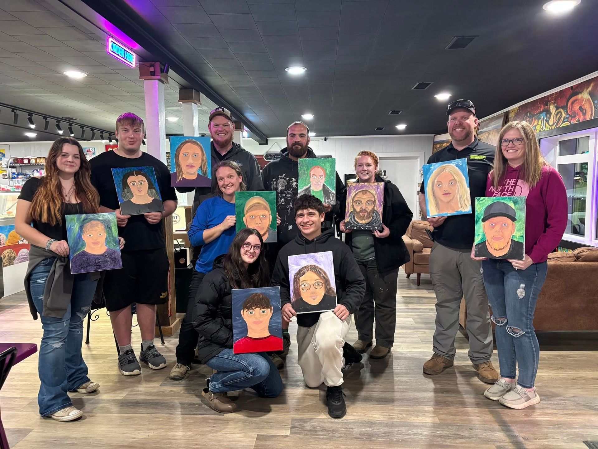Group of people holding up portraits they painted in a workshop. Inside, with neutral expressions.