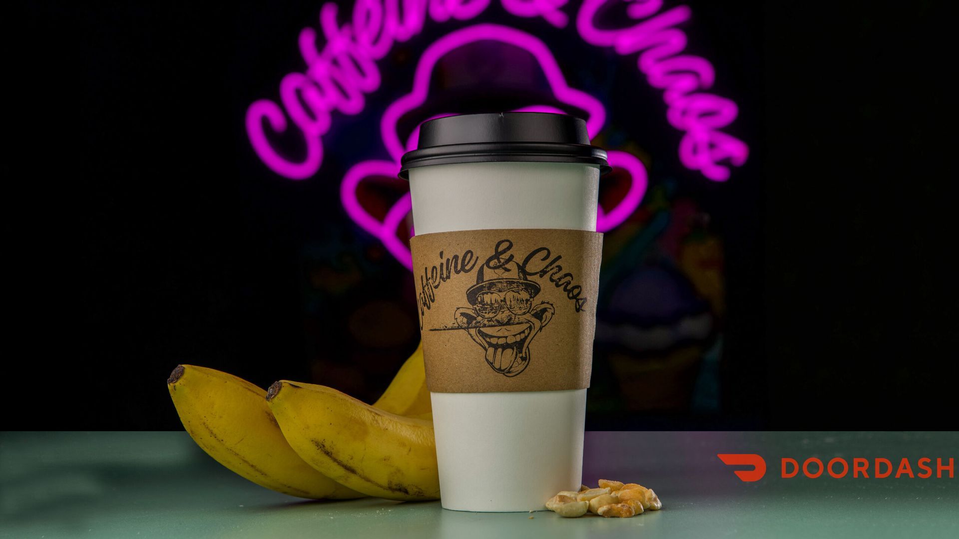 Coffee cup with sleeve, bananas, and a neon sign that says Caffeine & Chaos, DoorDash logo.