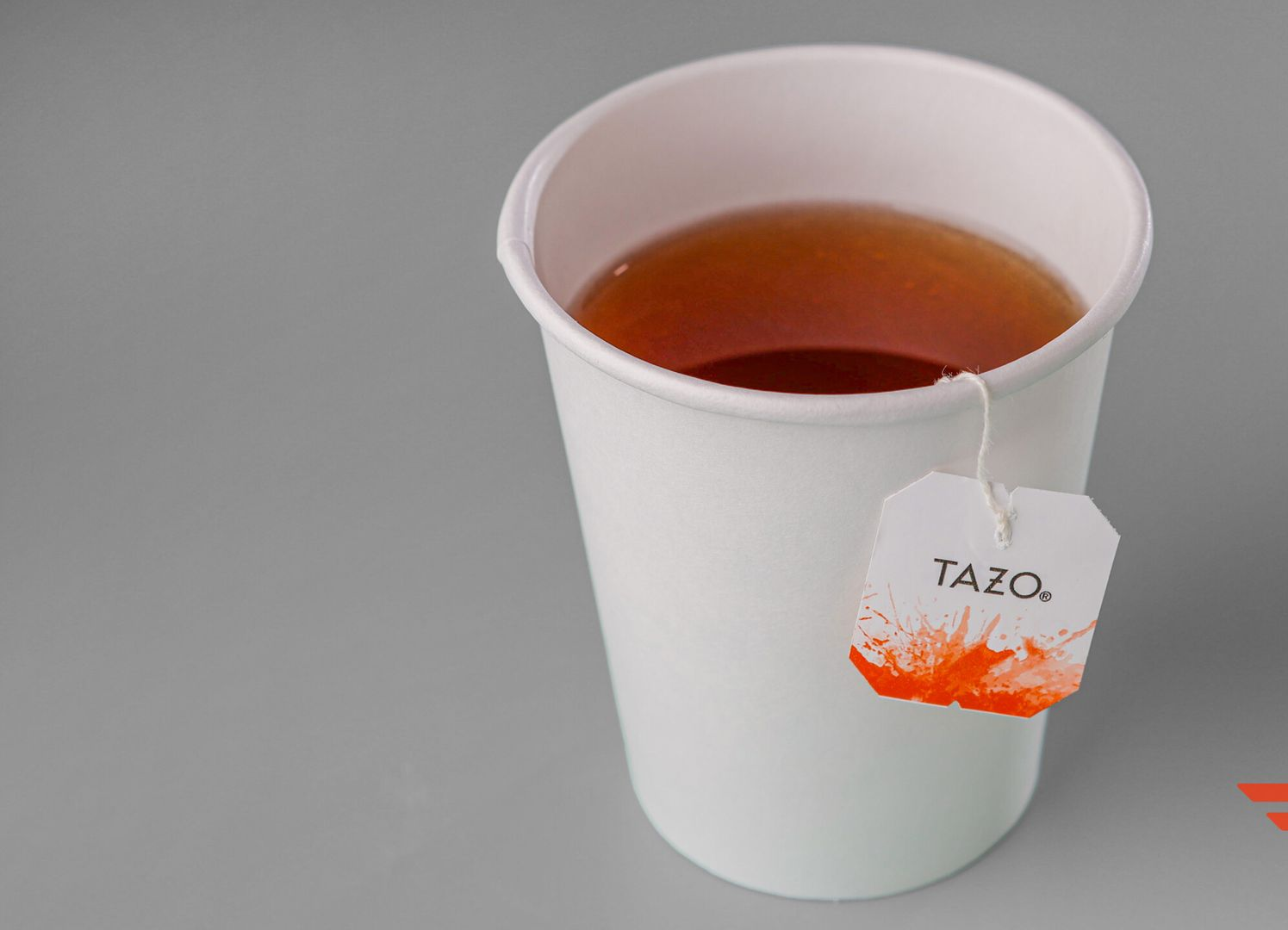 White paper cup of tea with Tazo tea bag, on a gray surface.