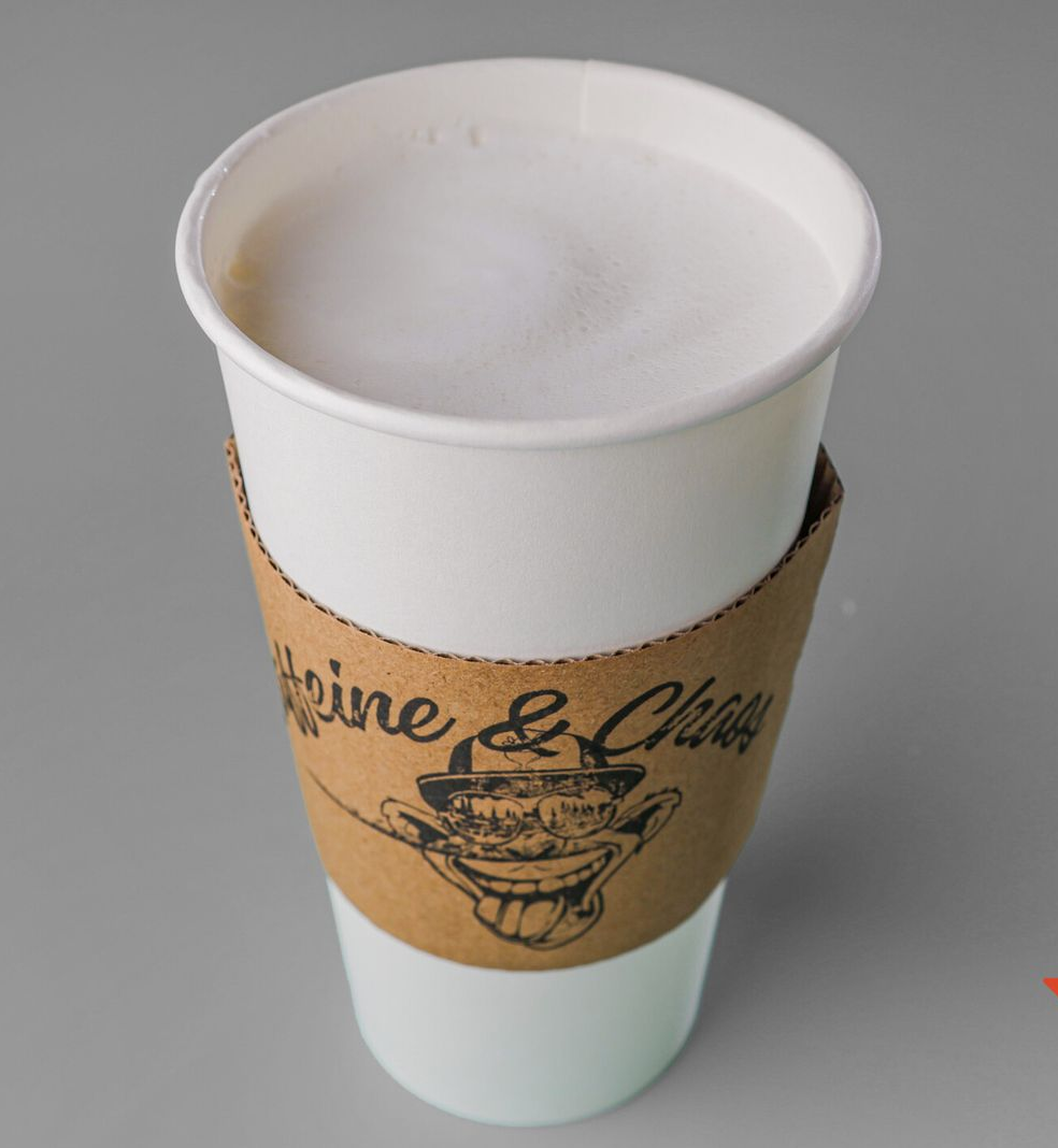 A white paper coffee cup with a brown sleeve, filled with a creamy beverage, on a gray surface.