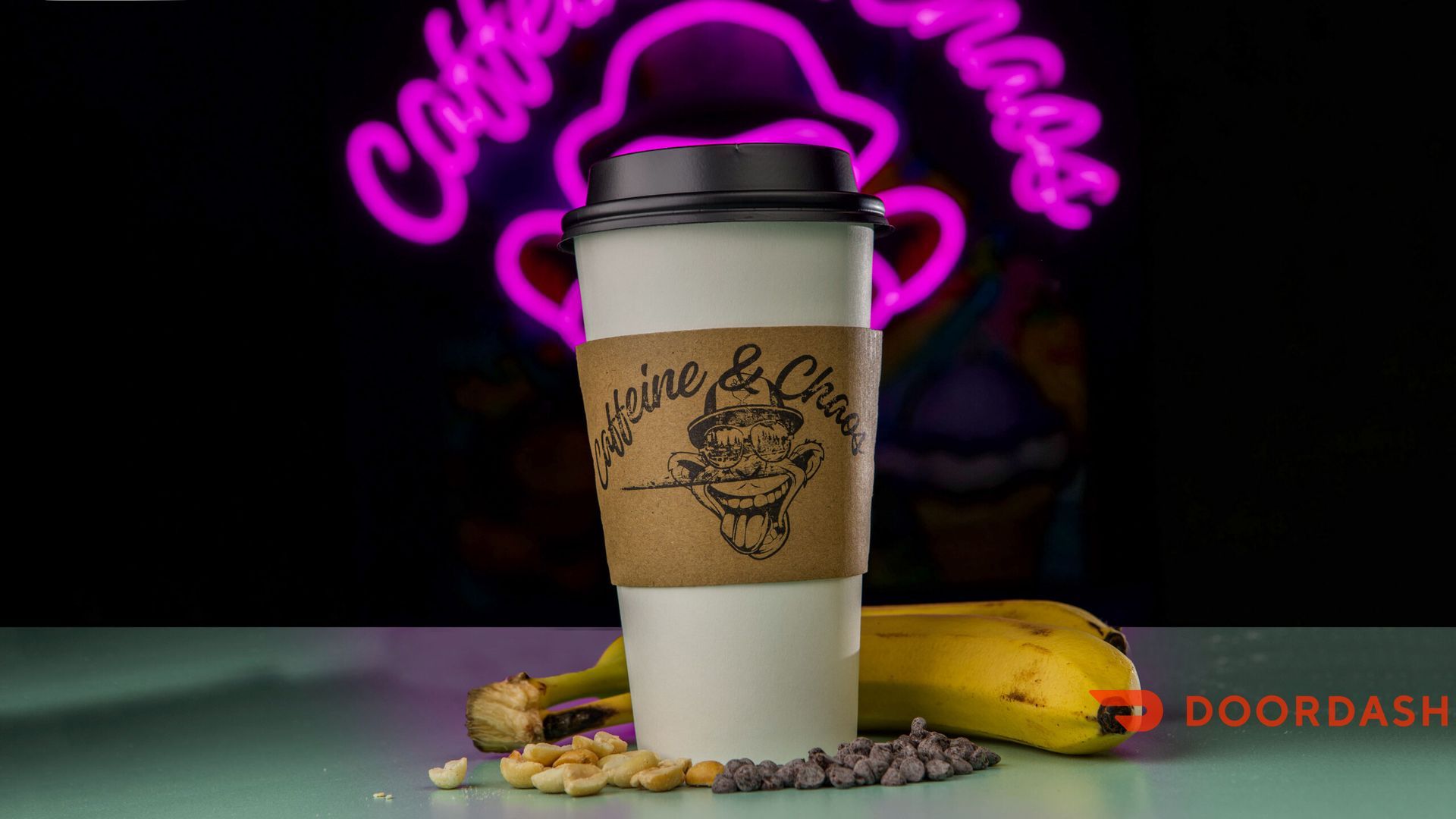 Cup of coffee with a sleeve, banana, nuts, and chocolate chips in front of a neon sign.