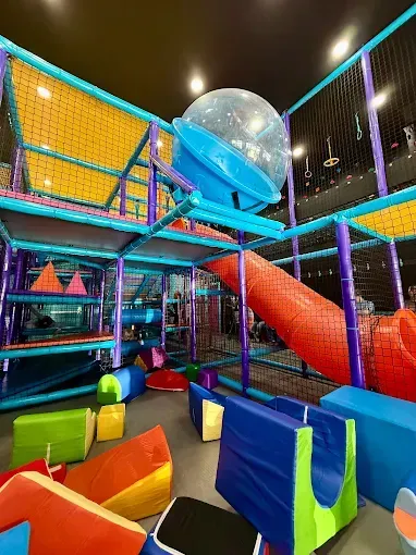 Indoor playground with colorful structures, slides, and soft play shapes.