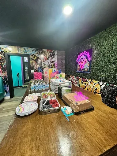 A table with food, drinks, and gifts in a party room with artwork.