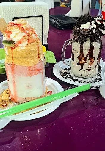 Two large, elaborate milkshakes on a purple table. One is strawberry and the other is Oreo.