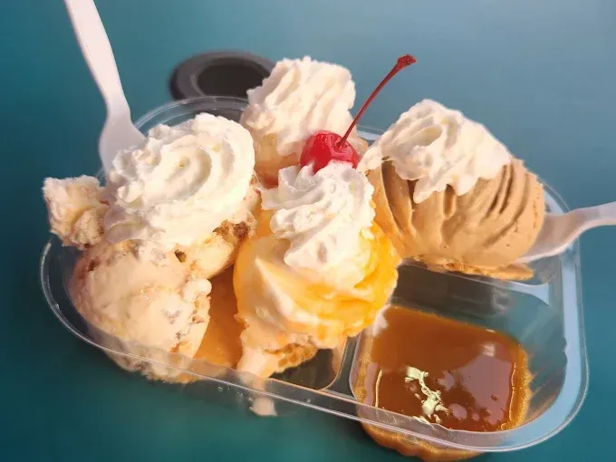 Ice cream sundae in a clear plastic container with caramel sauce and a cherry.