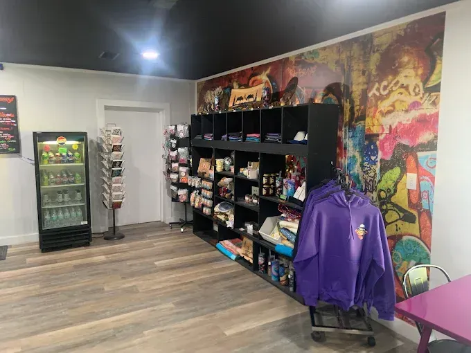 Interior of a store with snacks and drinks. A mural is on the wall. A purple hoodie hangs on a cart.