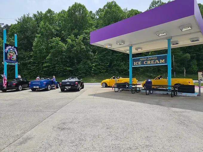 Cars parked at a gas station with purple and teal accents, including a sign that reads 