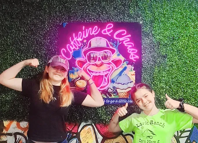 Two smiling people flex in front of a neon 