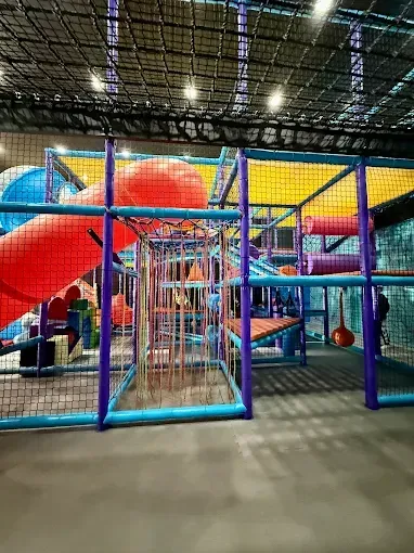 Indoor playground with colorful slides, tunnels, and climbing structures, all enclosed with safety netting.