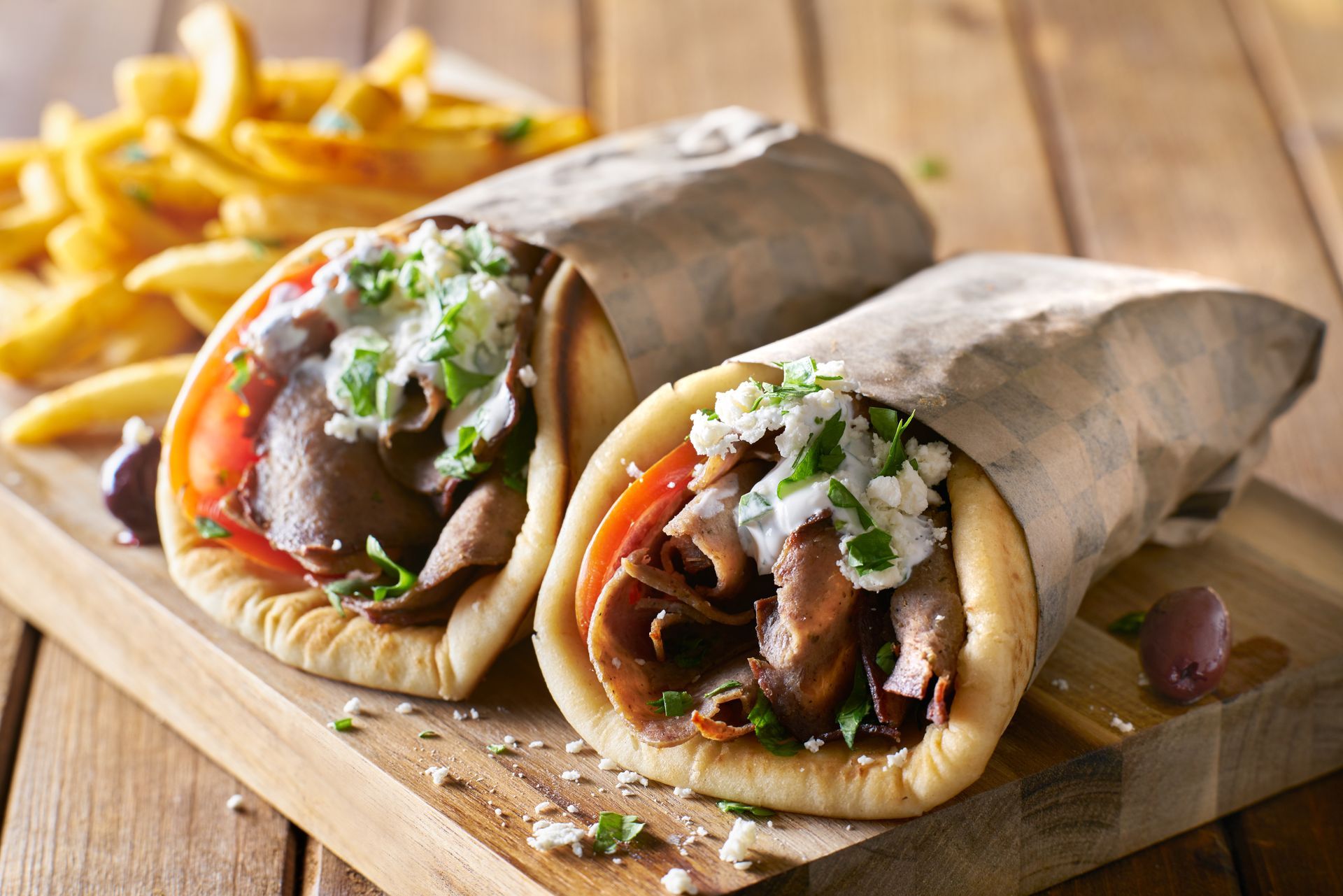 Two gyros and french fries on a wooden cutting board.