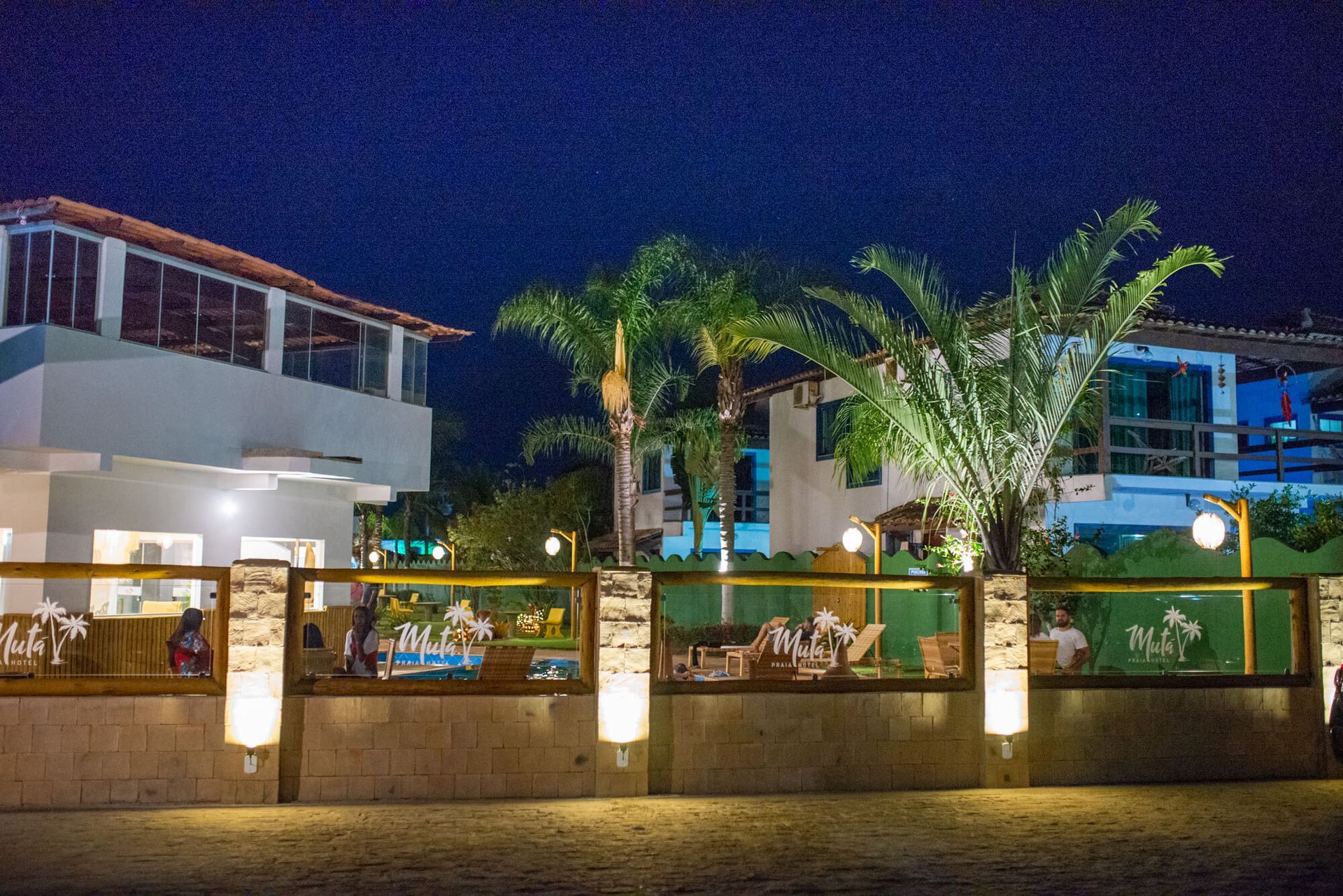 Uma cerca em volta de um prédio com palmeiras na frente à noite