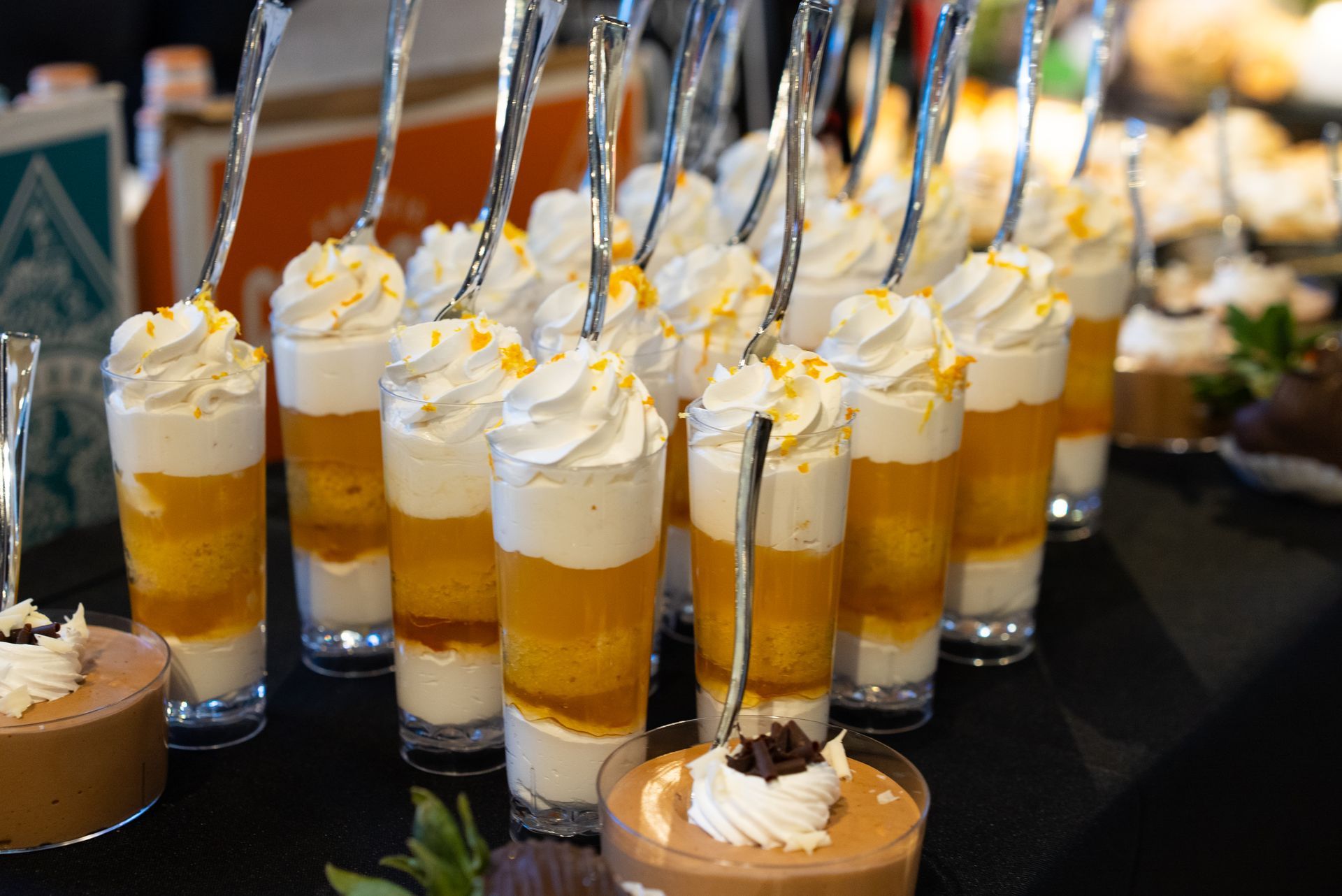 Glass desserts layered with yellow and white filling, topped with whipped cream and orange zest.