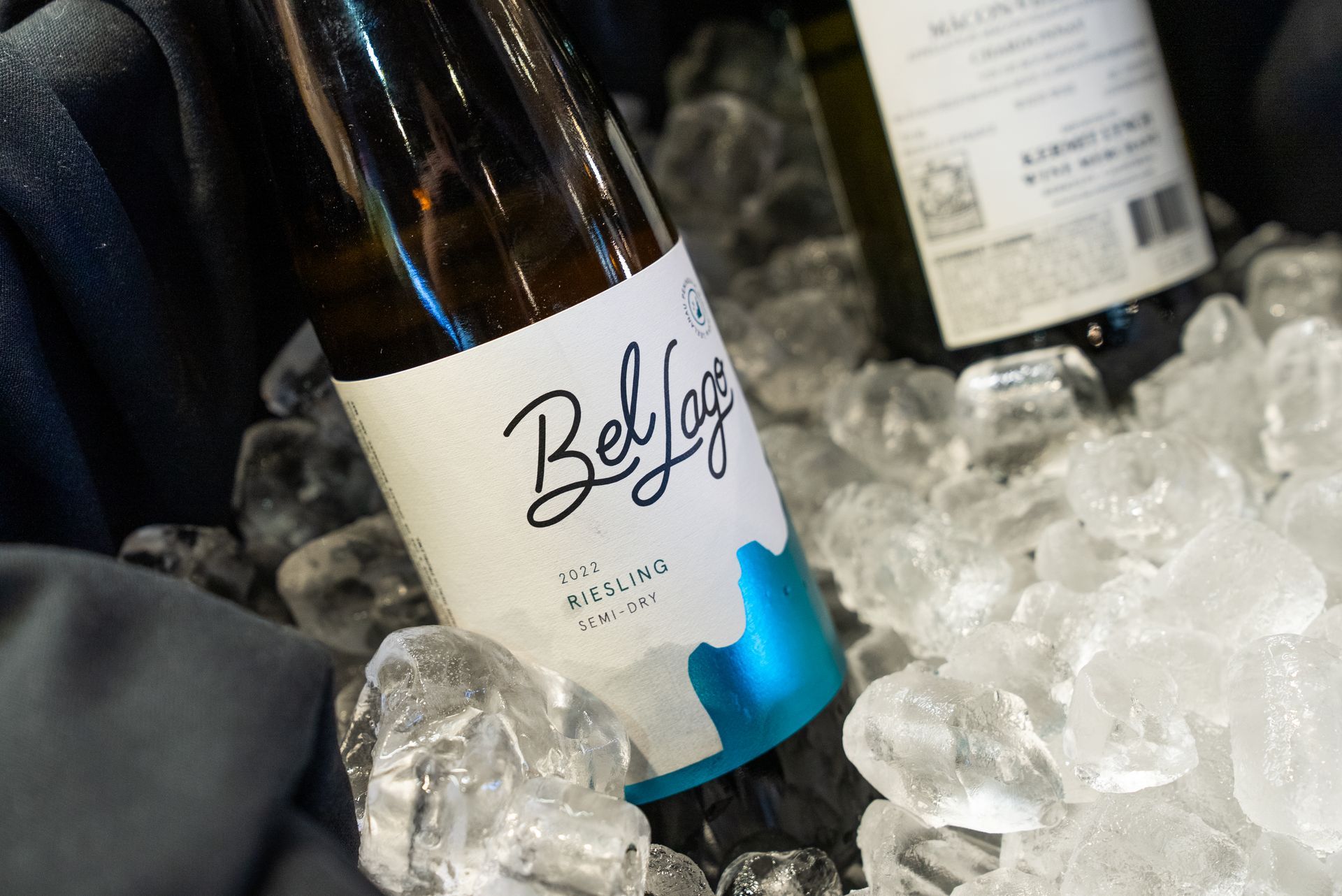 Bottles of white wine in a bed of ice. One bottle has a blue and white label that reads “Belfry”.