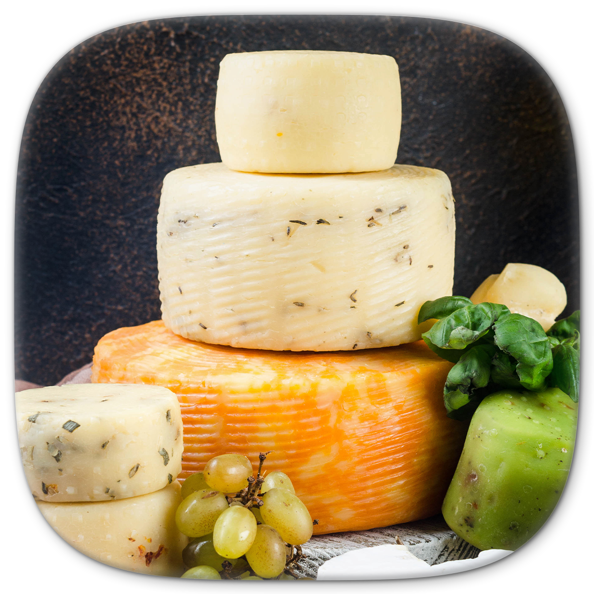 Cheese wheels stacked in a tower, with grapes and basil on the side.