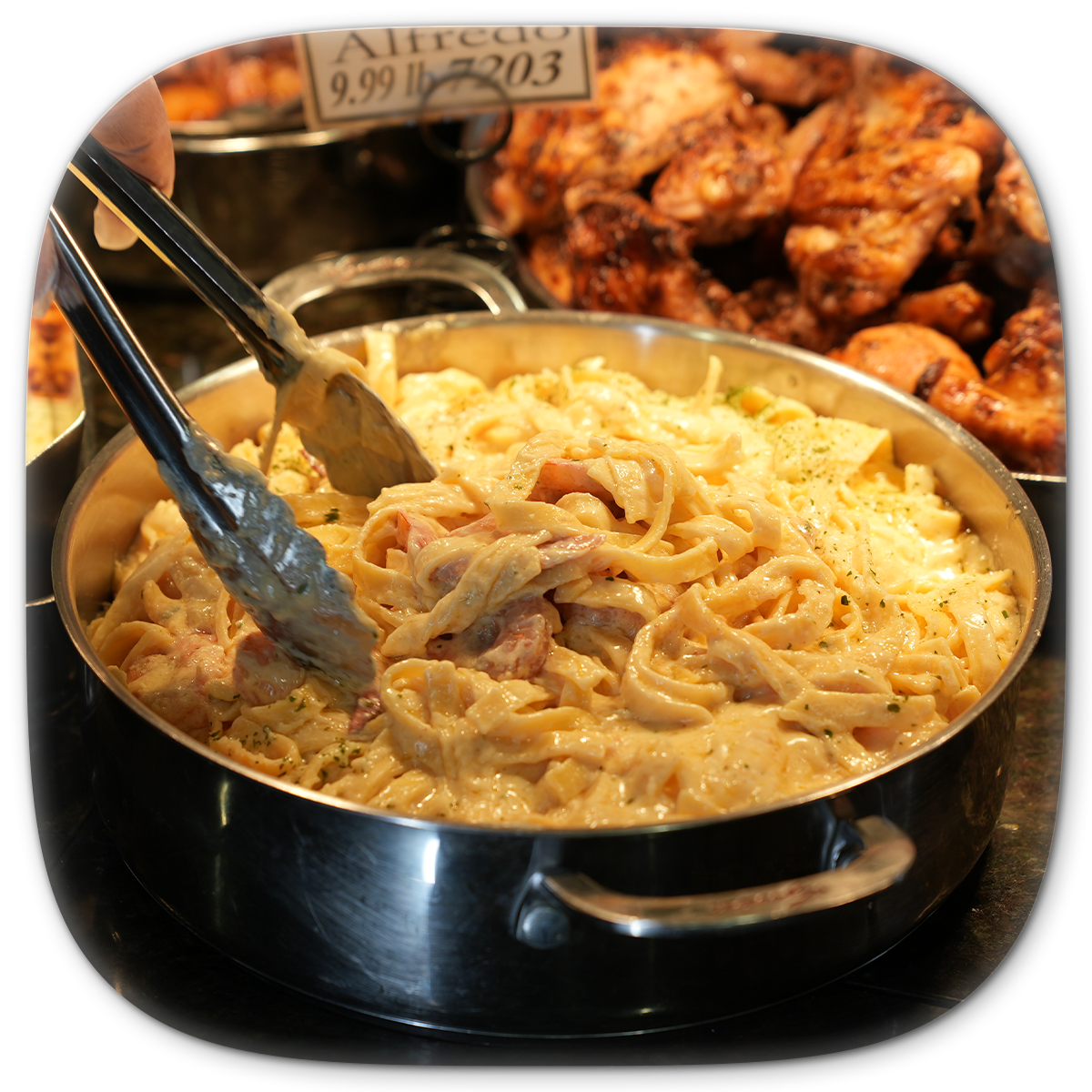 Pasta Alfredo being served with tongs from a stainless steel pan.