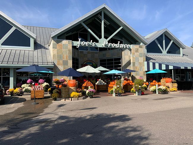 Joe's Produce storefront with fall pumpkins, flowers, and umbrellas under a blue sky.