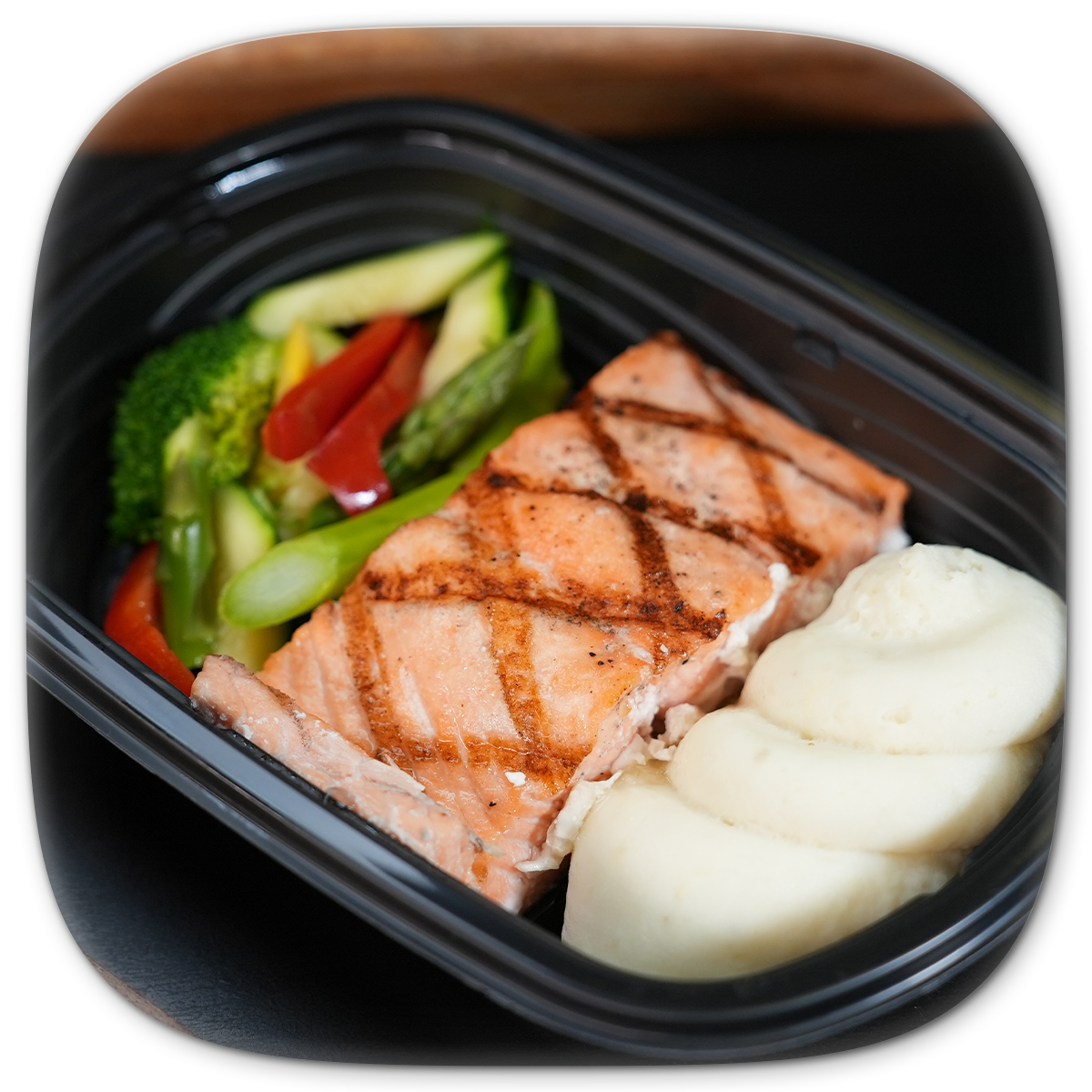 Grilled salmon meal with vegetables and mashed potatoes in a black container.