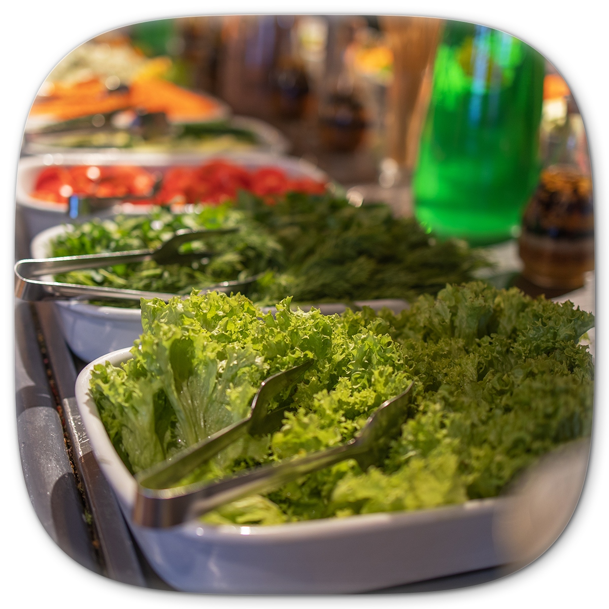 Salad bar with fresh green lettuce and other vegetables in white serving dishes.