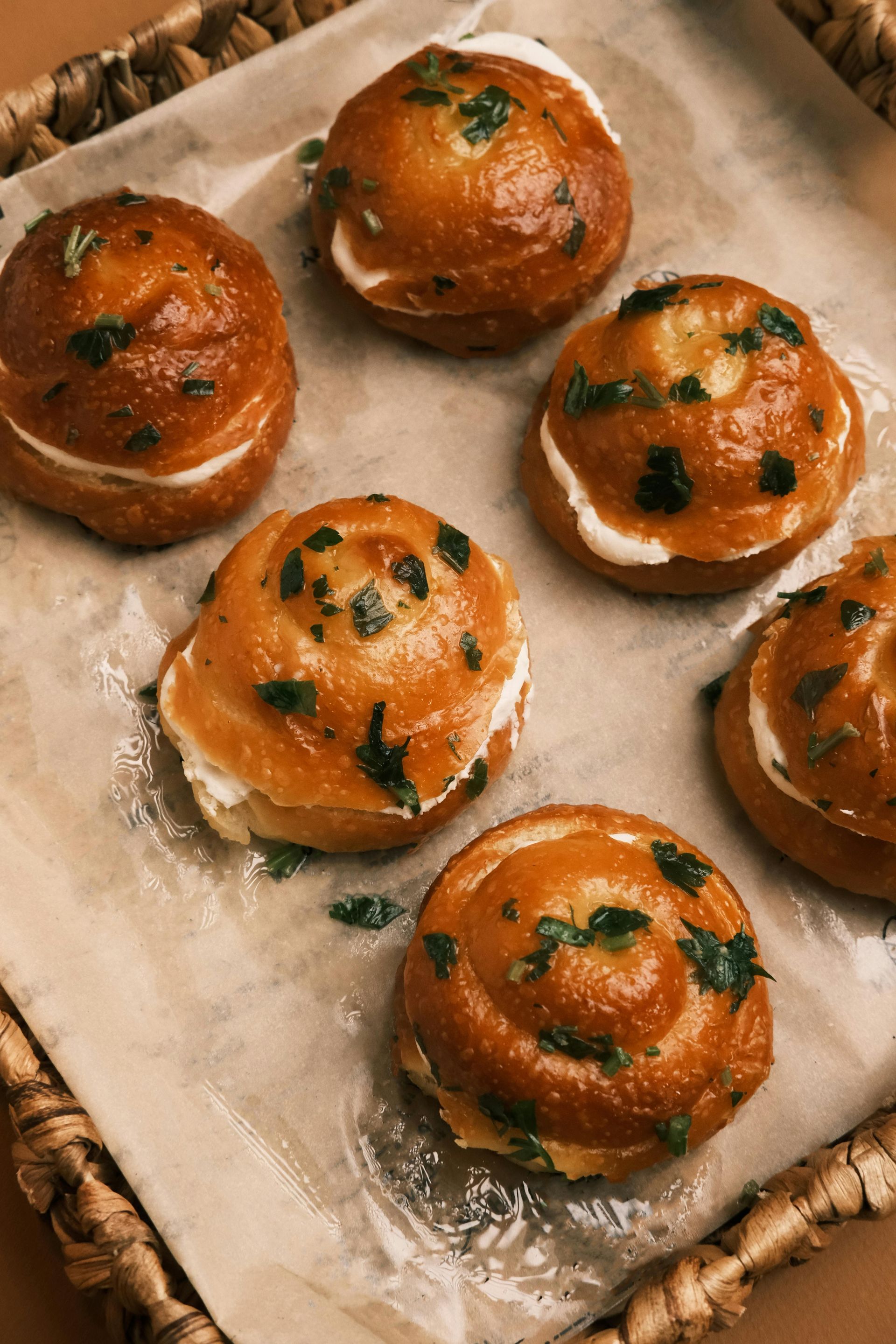 Six round rolls with creamy filling and parsley, on parchment paper in a wicker basket.