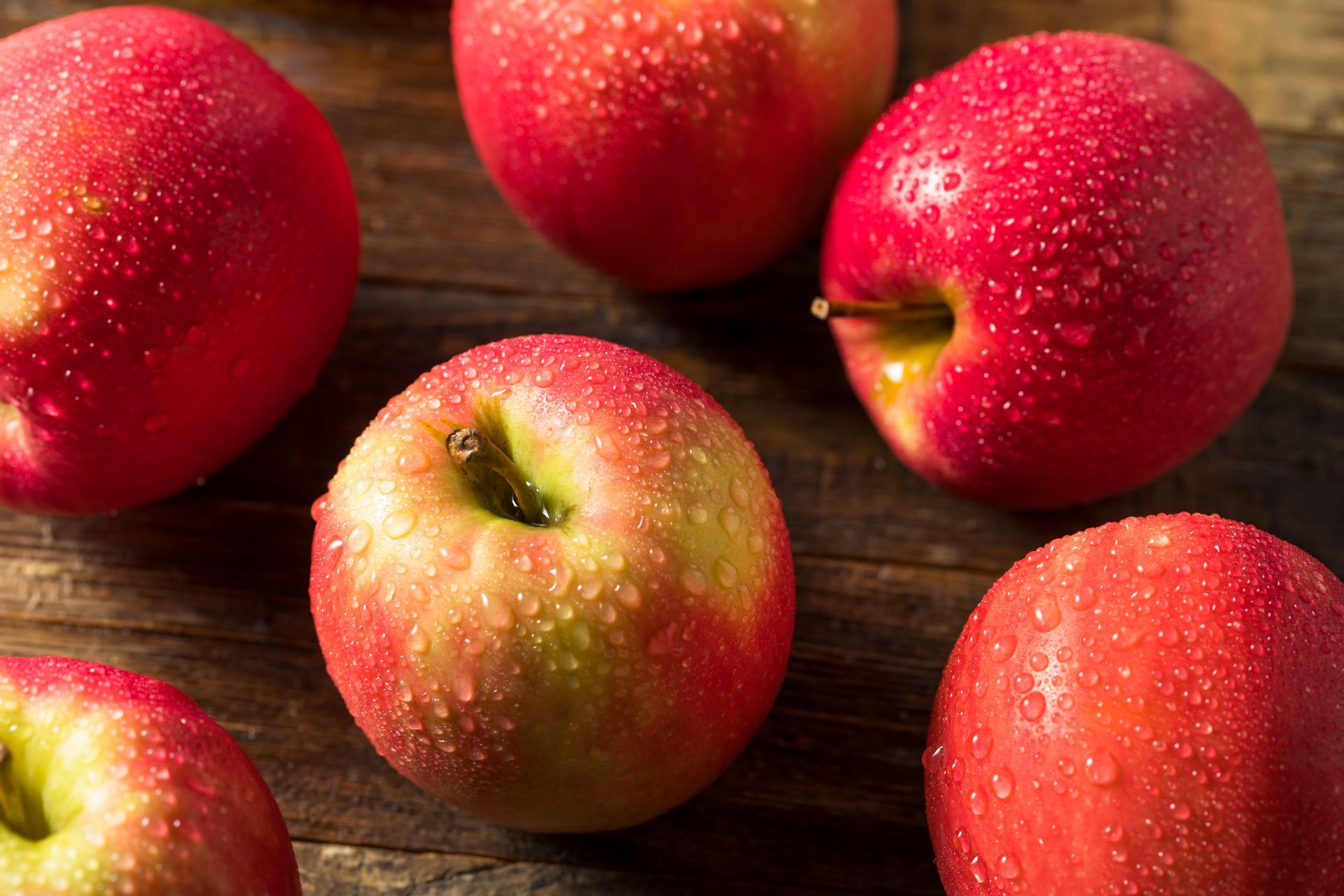 Close-up of red apples with water droplets on a wooden surface.
