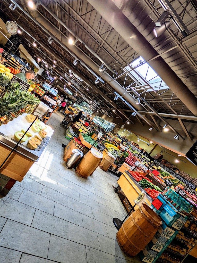 Produce aisle in a grocery store, displaying fresh produce. Wooden barrels, various fruits and vegetables.