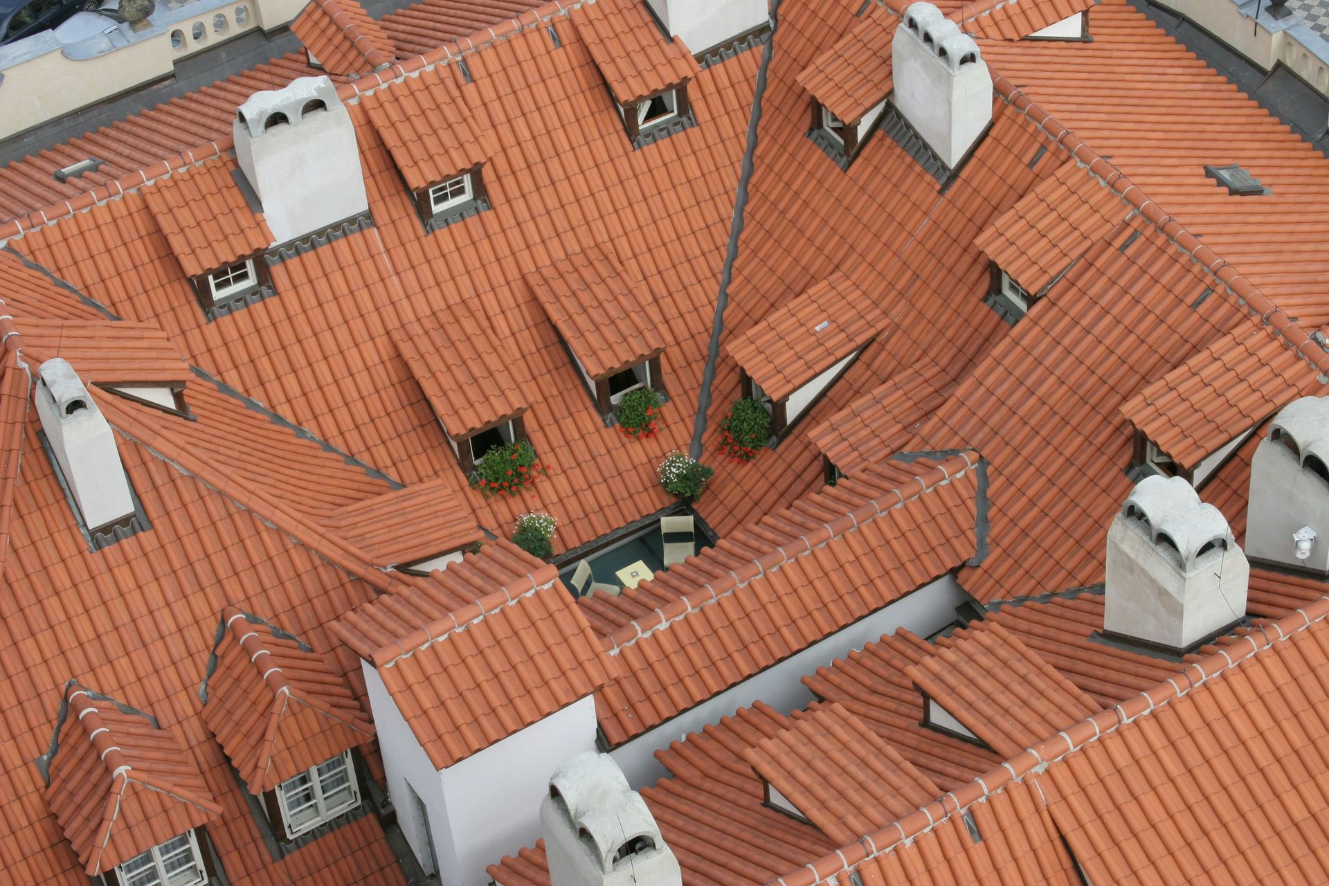 An aerial view of multiple terracotta-tiled rooftops featuring various chimneys, dormer windows, and a small courtyard.