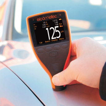 Una persona sostiene un dispositivo elcometer frente a un automóvil