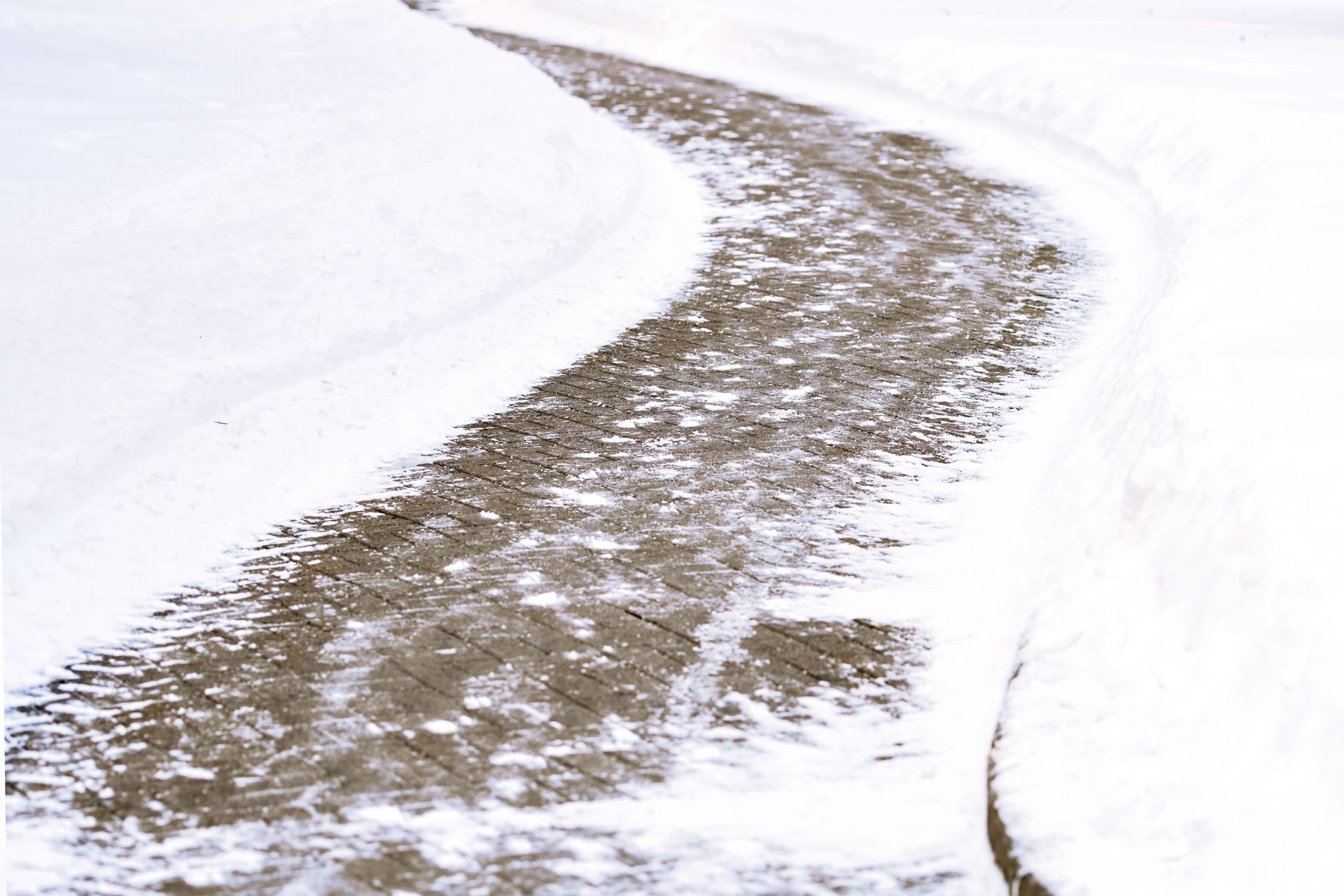 A snowy road with tire tracks on the side of it.
