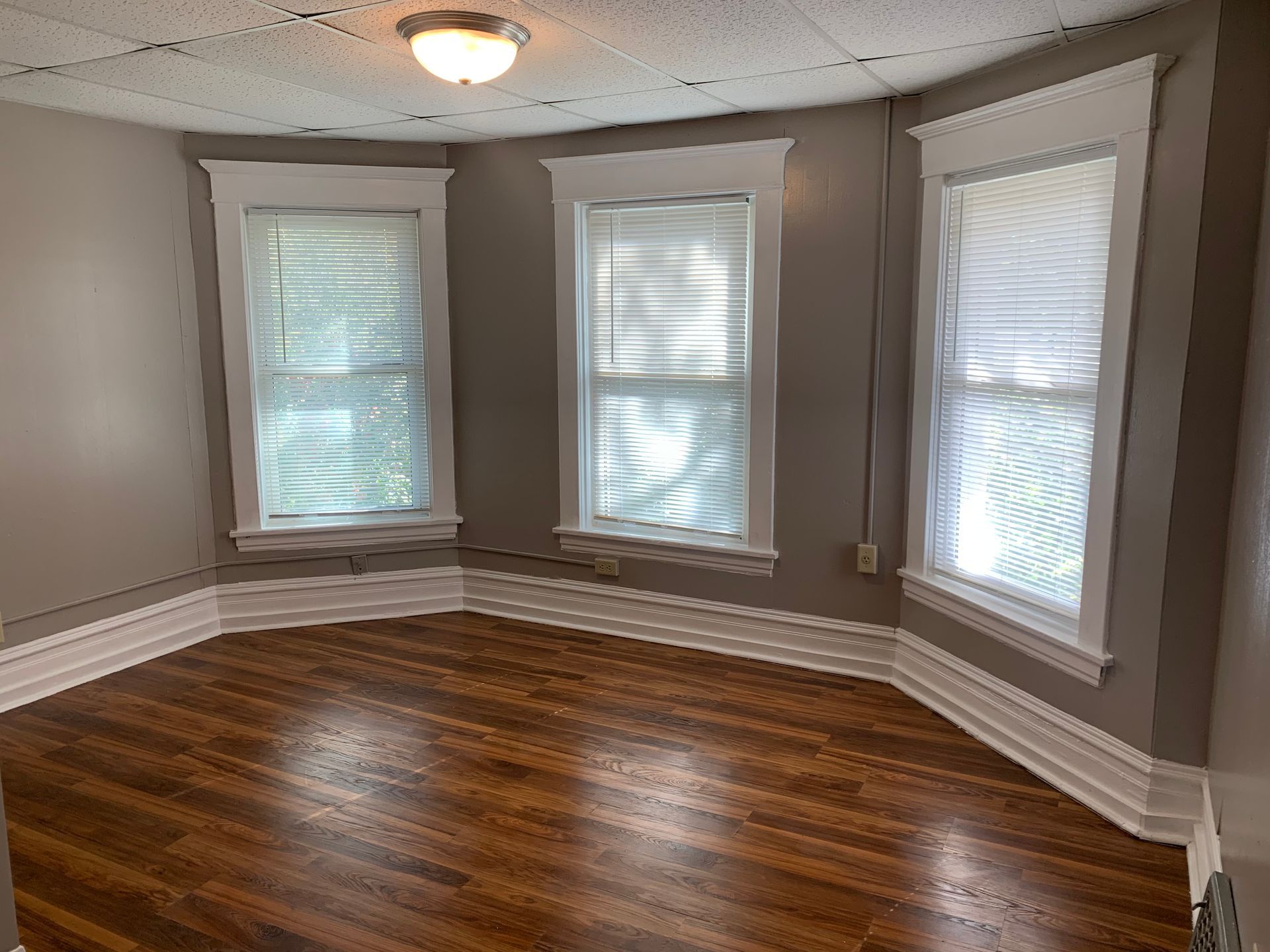An empty room with hardwood floors and three windows.