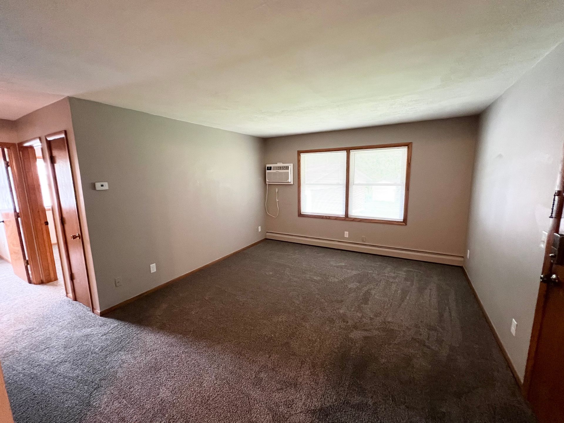 An empty living room with a window and air conditioner.
