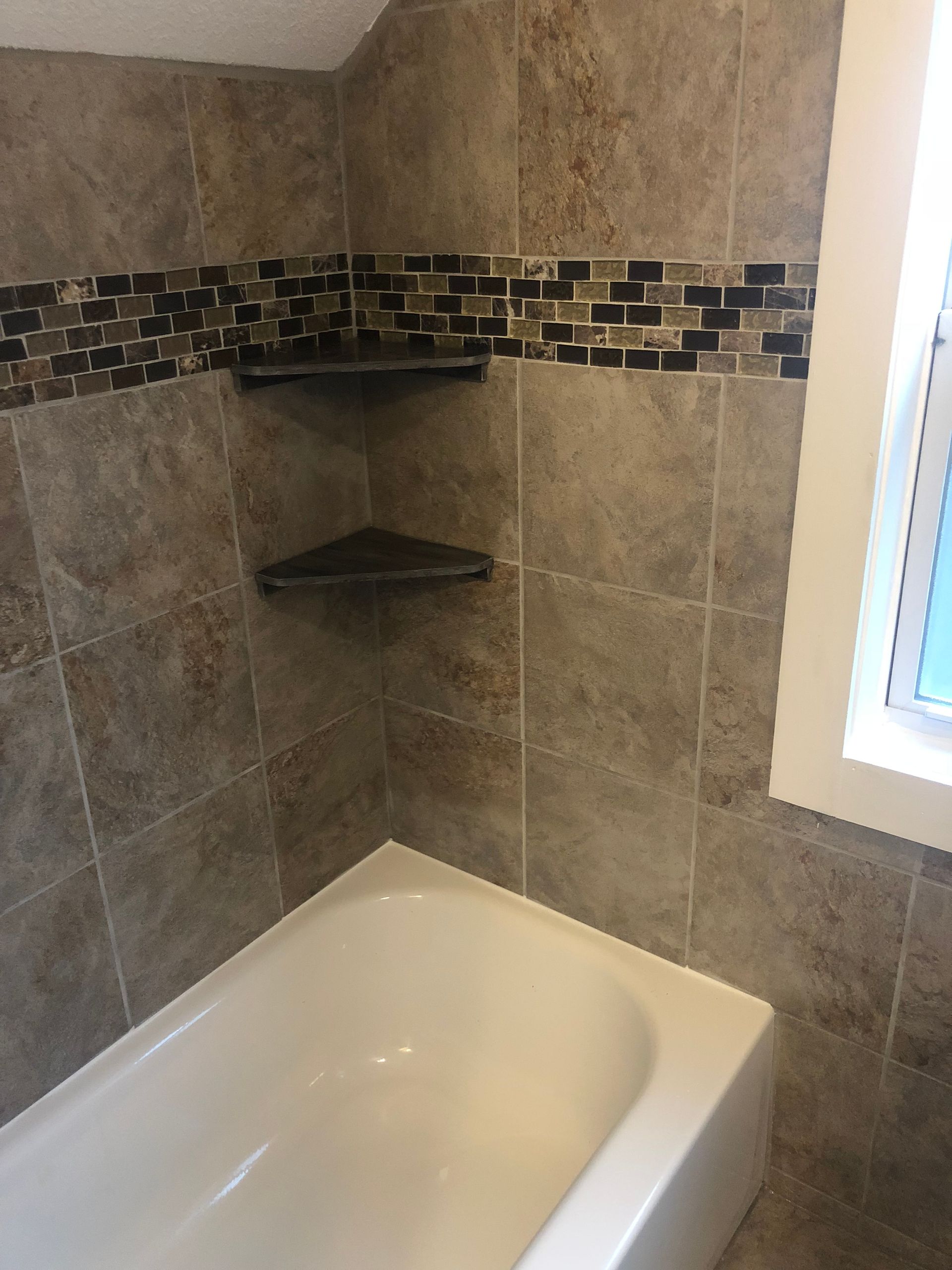 A bathtub in a bathroom with tiled walls and a window.