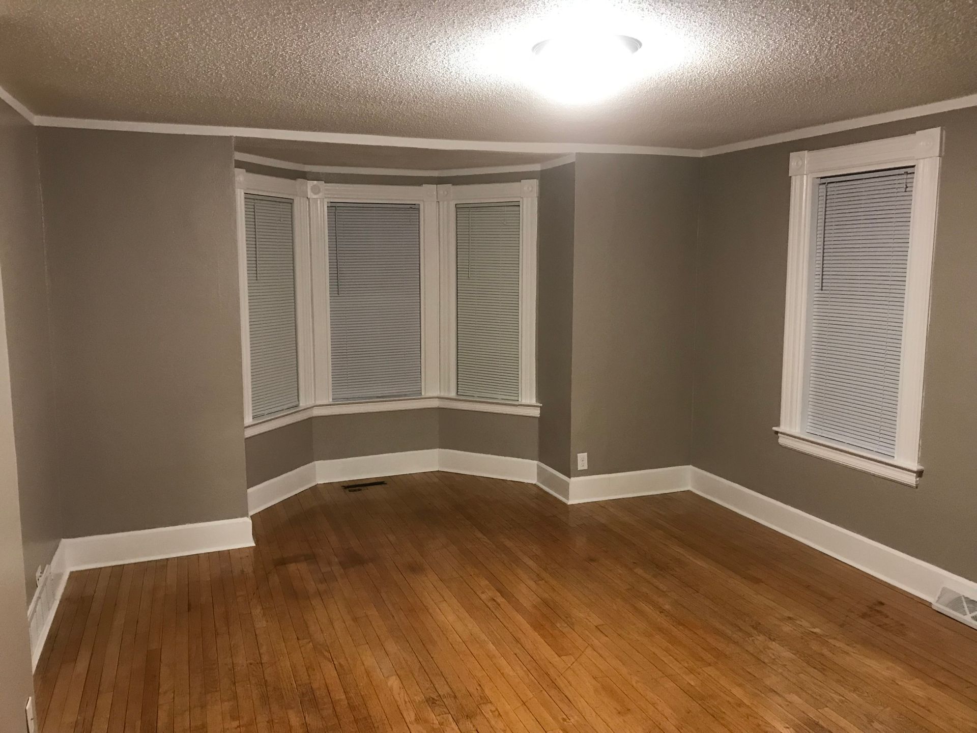 An empty living room with a bay window and hardwood floors.