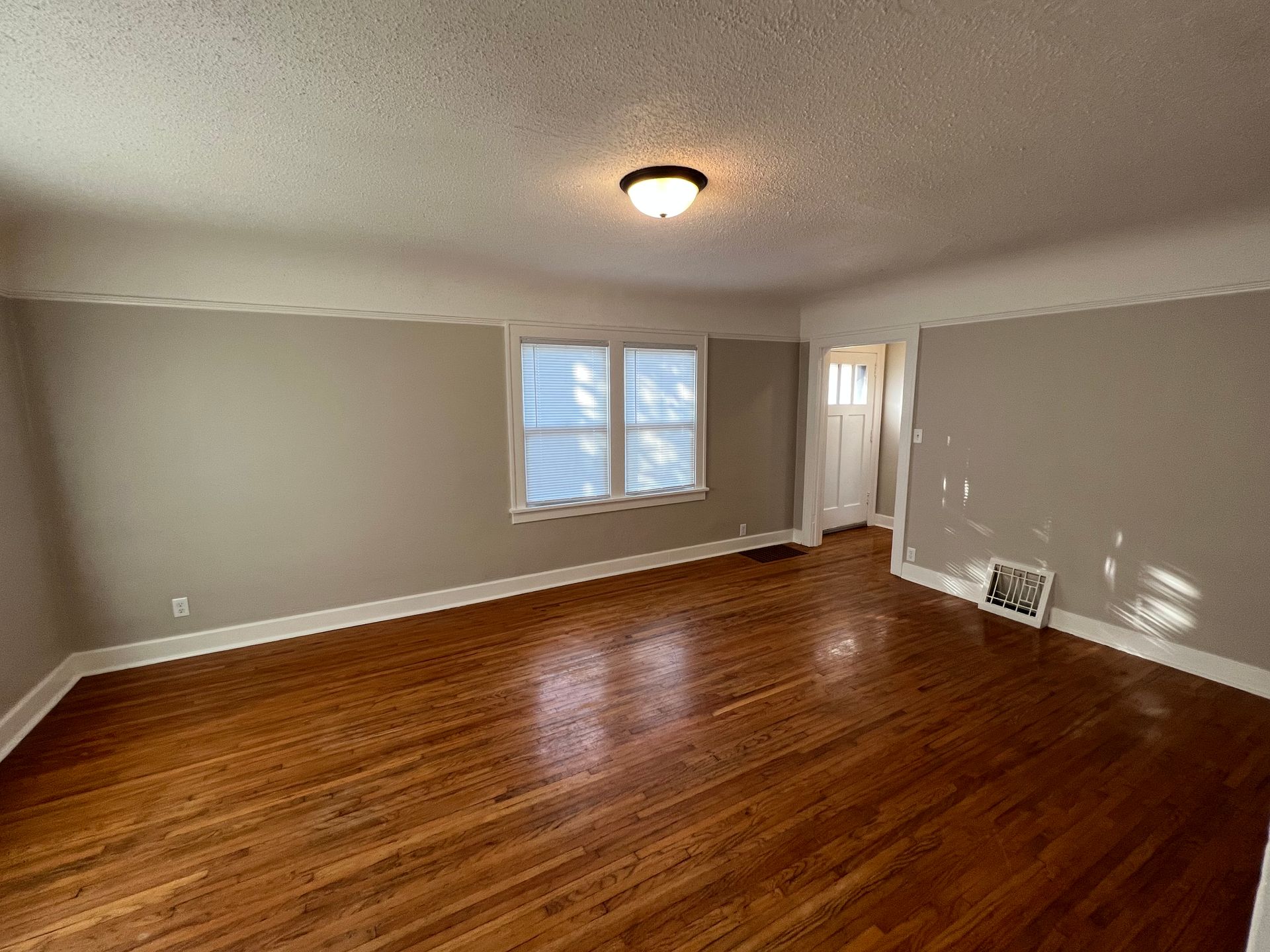 An empty living room with hardwood floors and two windows.