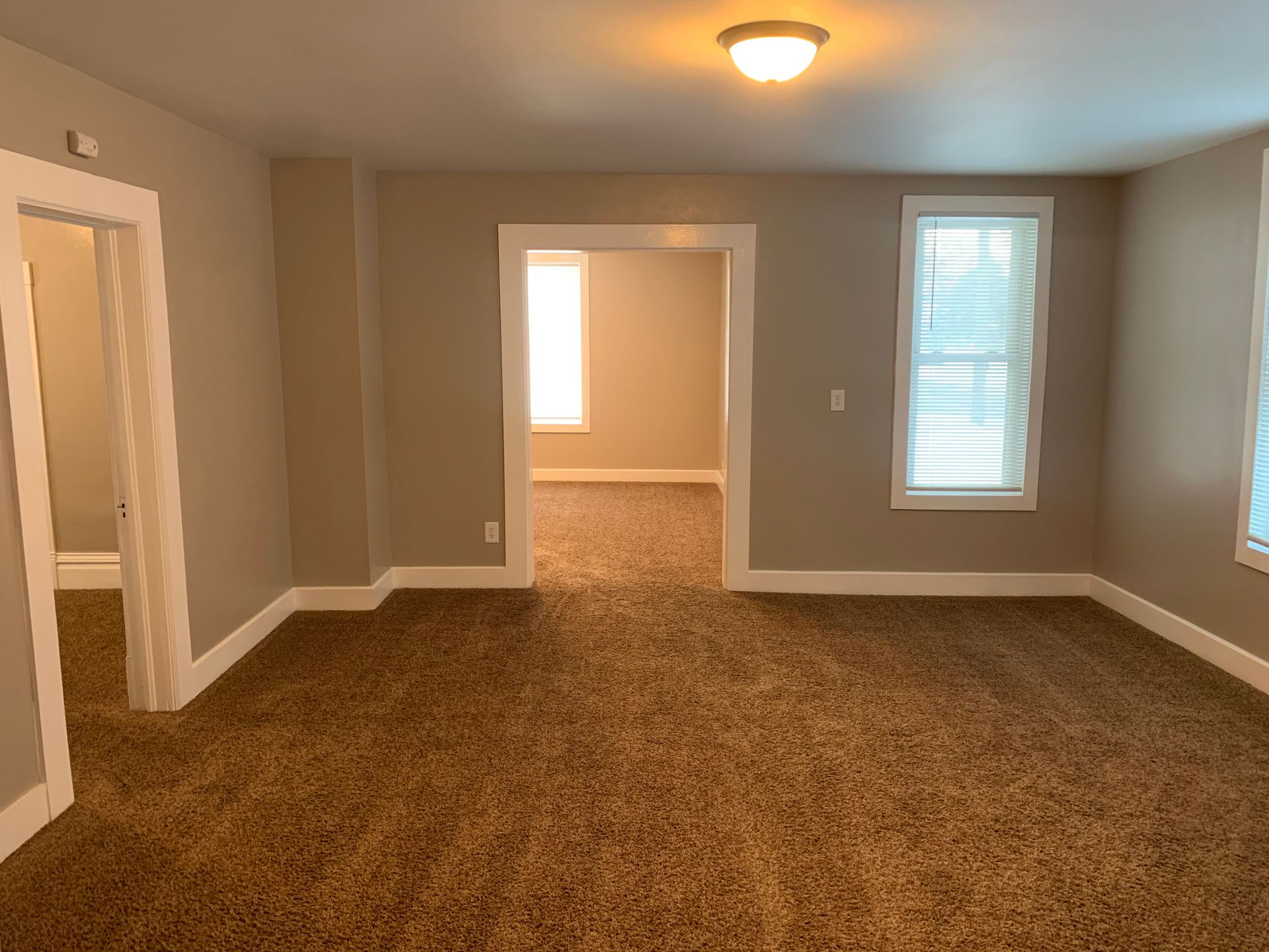 An empty living room with a brown carpet and two windows.