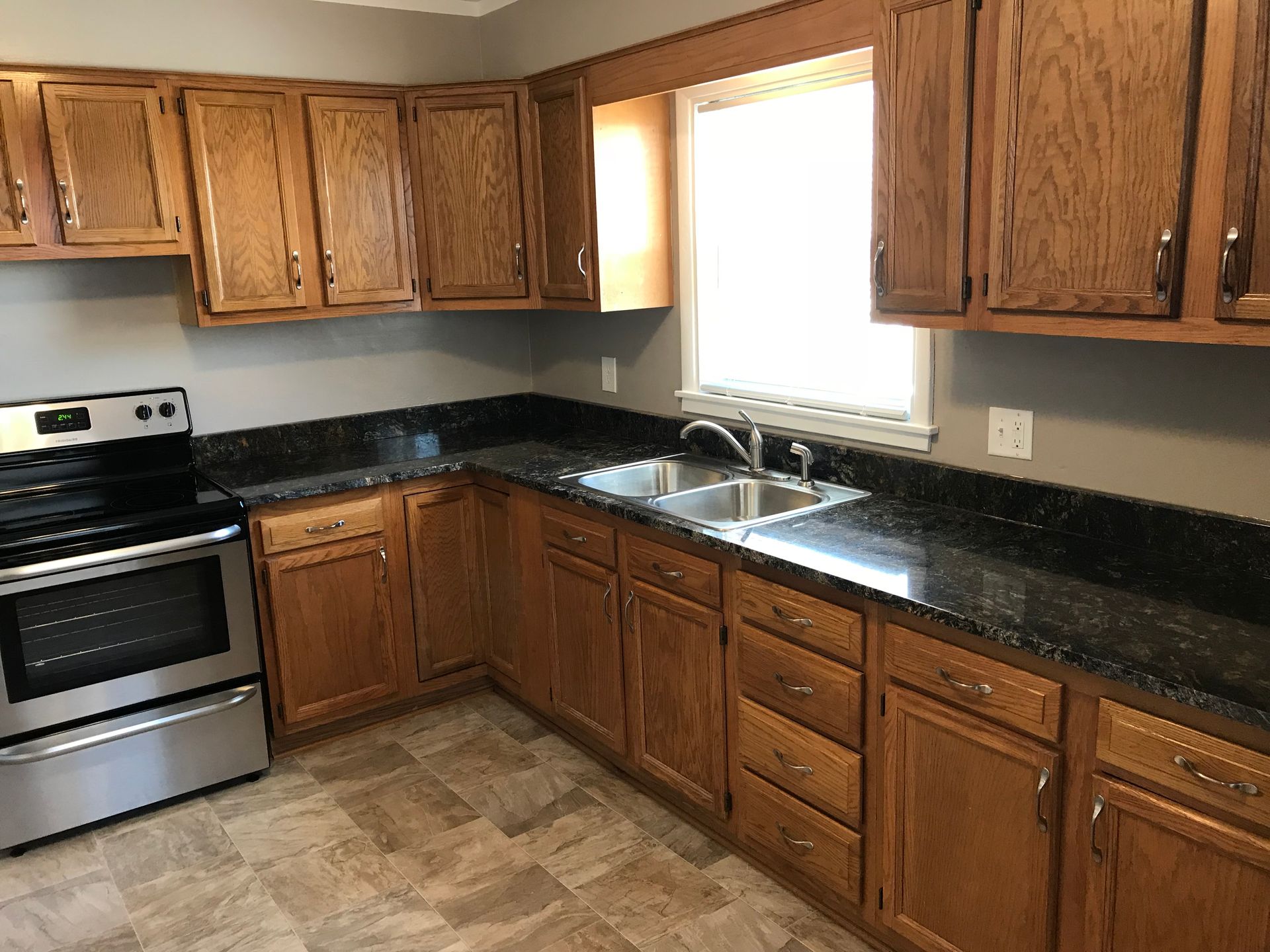 A kitchen with wooden cabinets , granite counter tops , a stove and a sink.