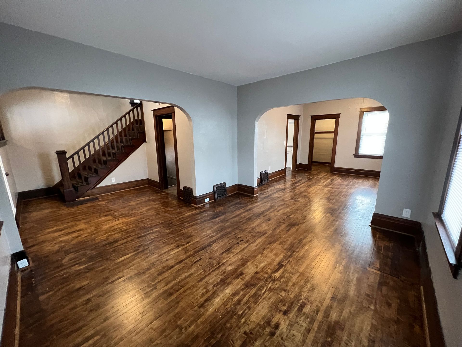 An empty living room with hardwood floors and a staircase.