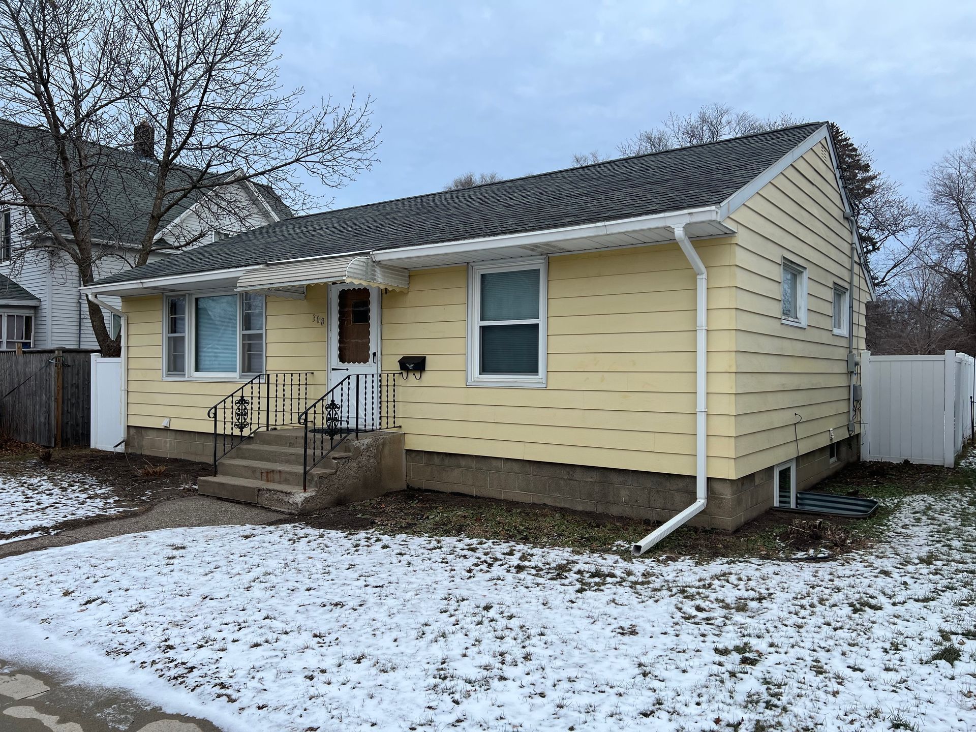 A small yellow house with snow on the ground in front of it.