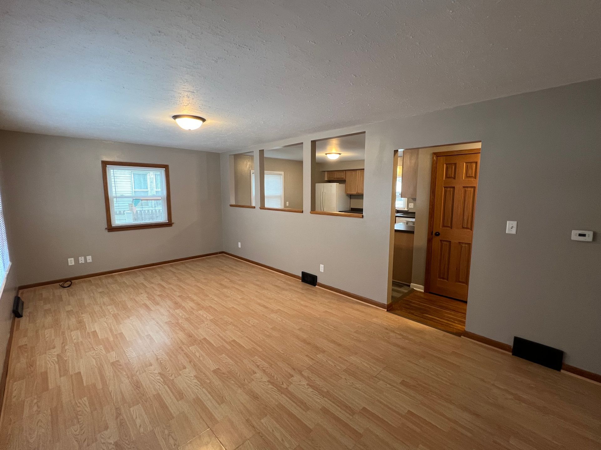 An empty living room with hardwood floors and a kitchen in the background.