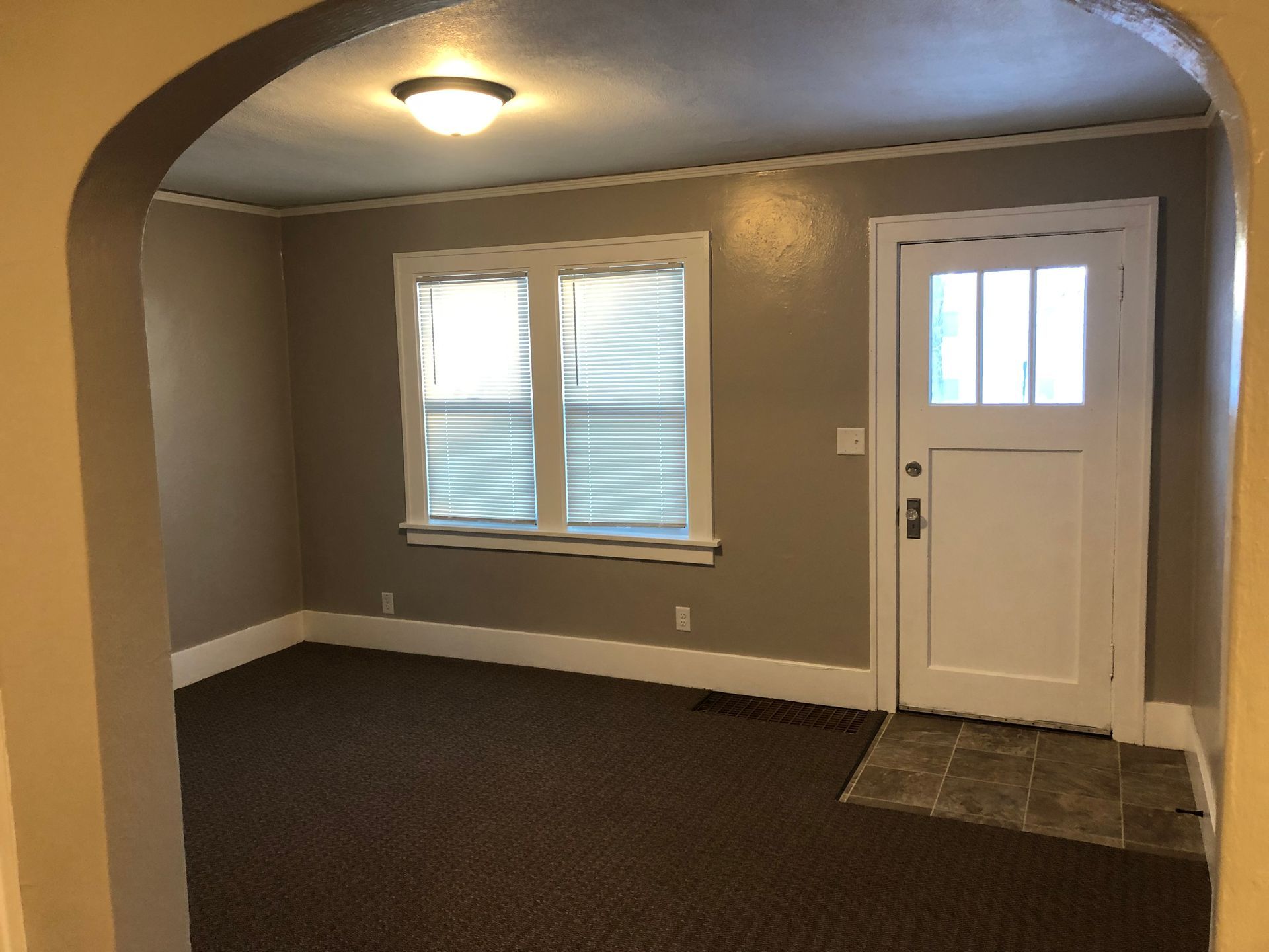 An empty living room with a white door and two windows.