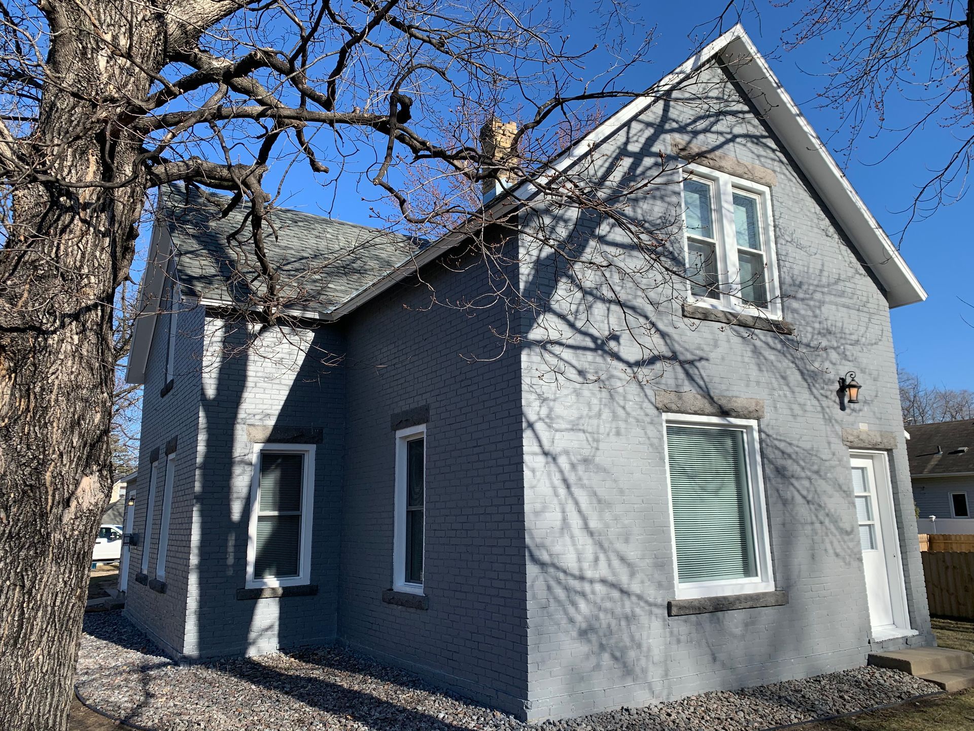 A gray house with a tree in front of it on a sunny day.