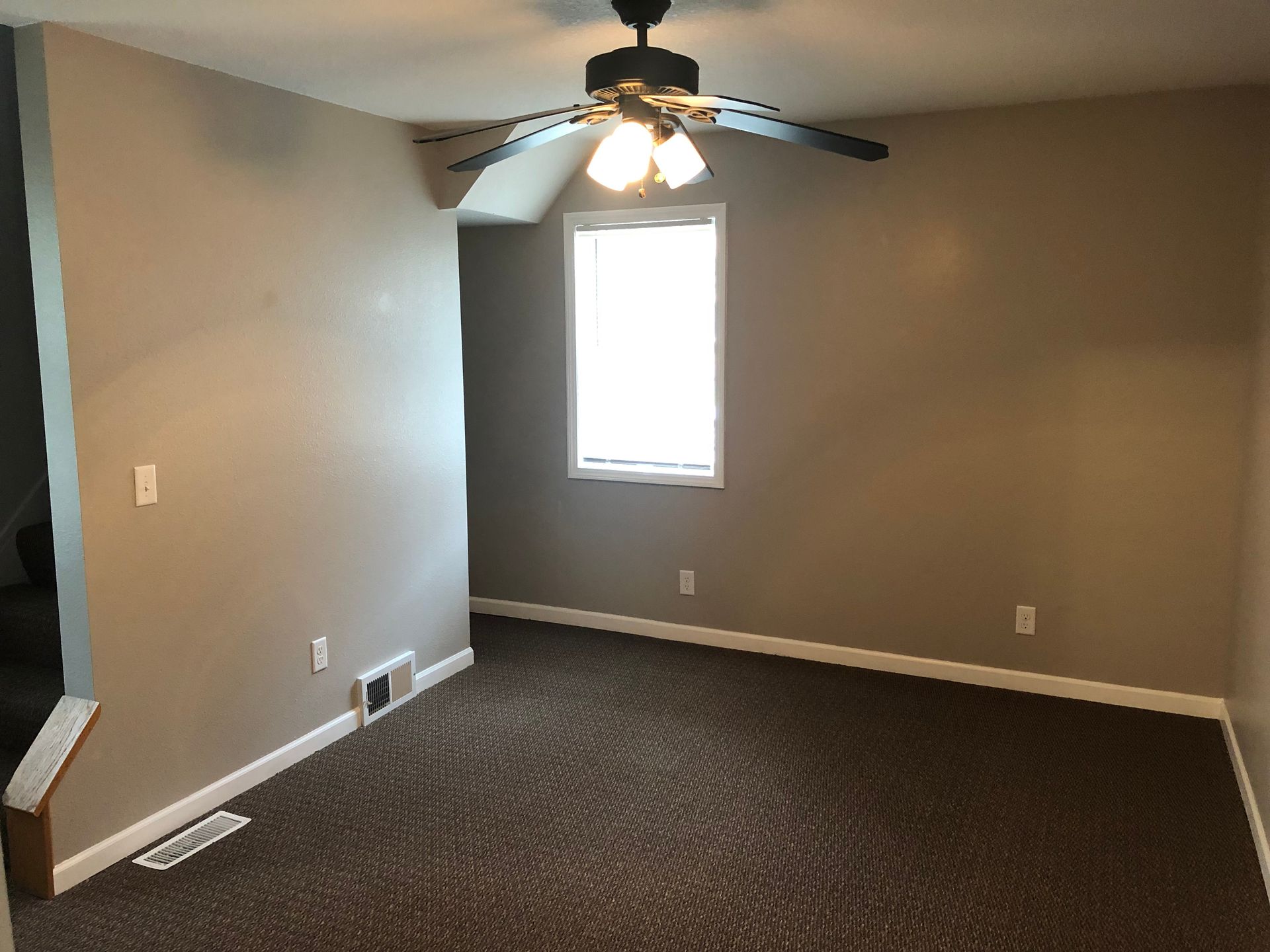 An empty living room with a ceiling fan and a window.