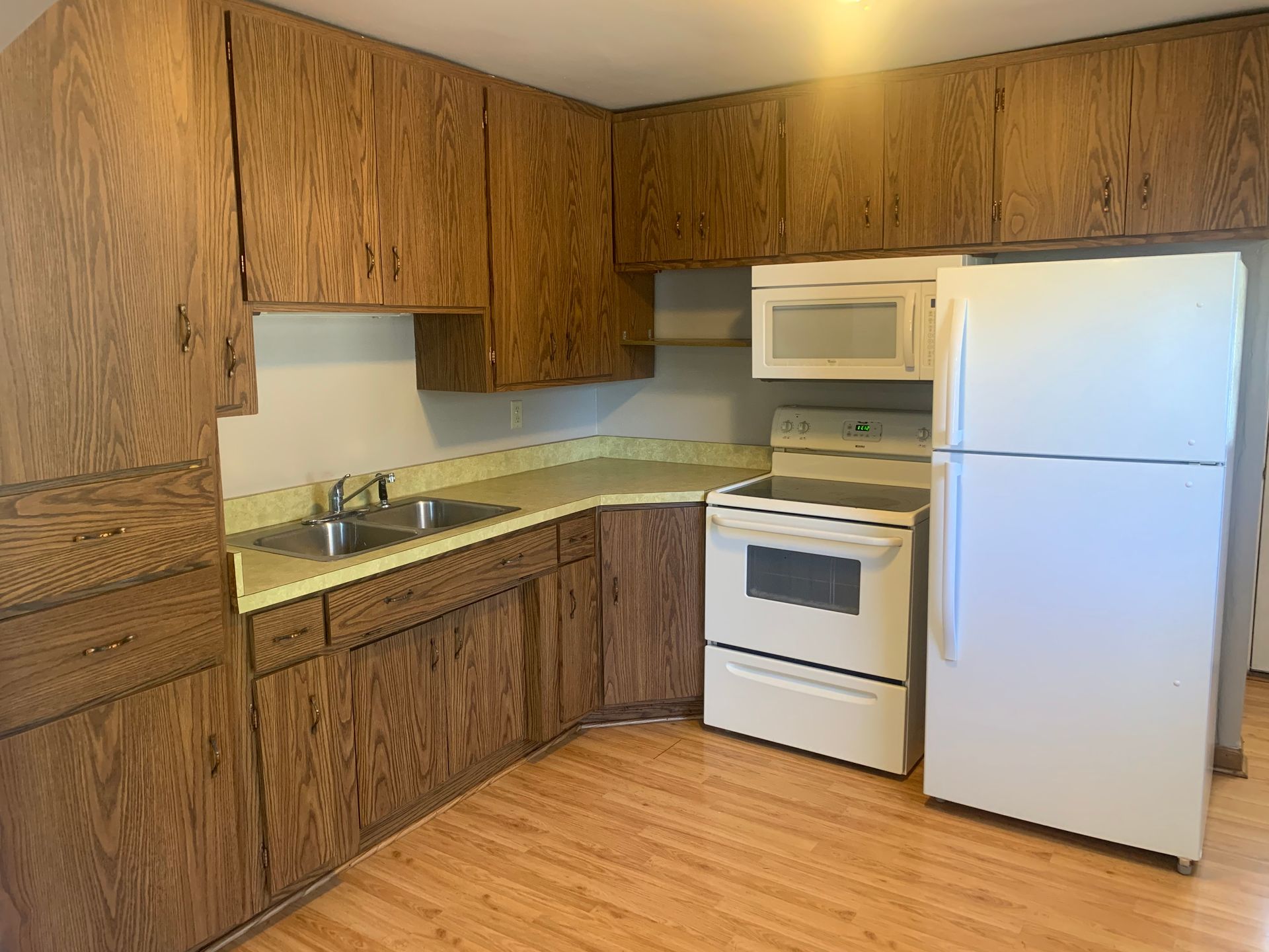 A kitchen with wooden cabinets , a white refrigerator , stove and microwave.