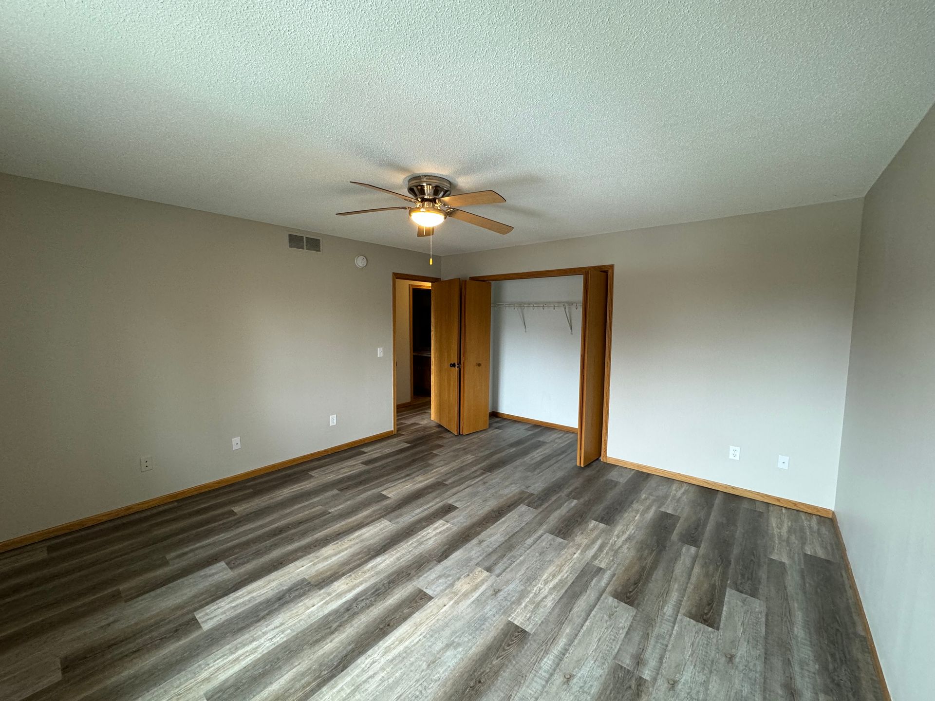 An empty bedroom with hardwood floors and a ceiling fan.
