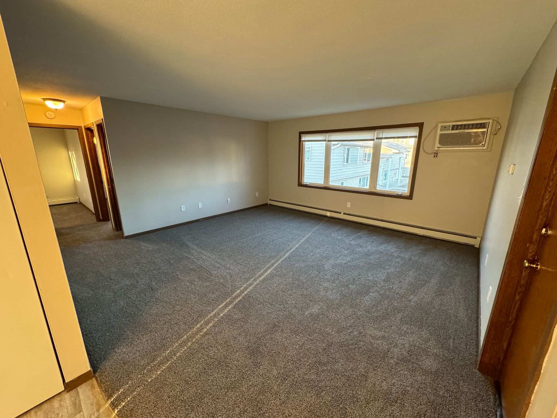 An empty living room with a carpeted floor and a window.