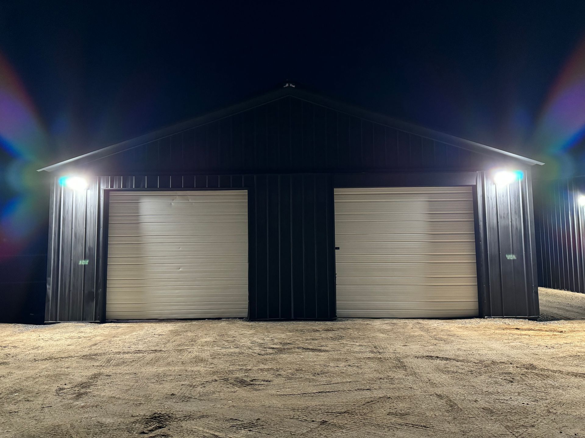 A garage with two garage doors is lit up at night.