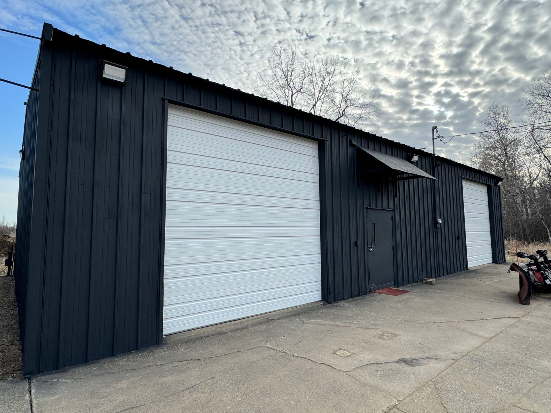 A black building with white garage doors and a motorcycle parked in front of it.