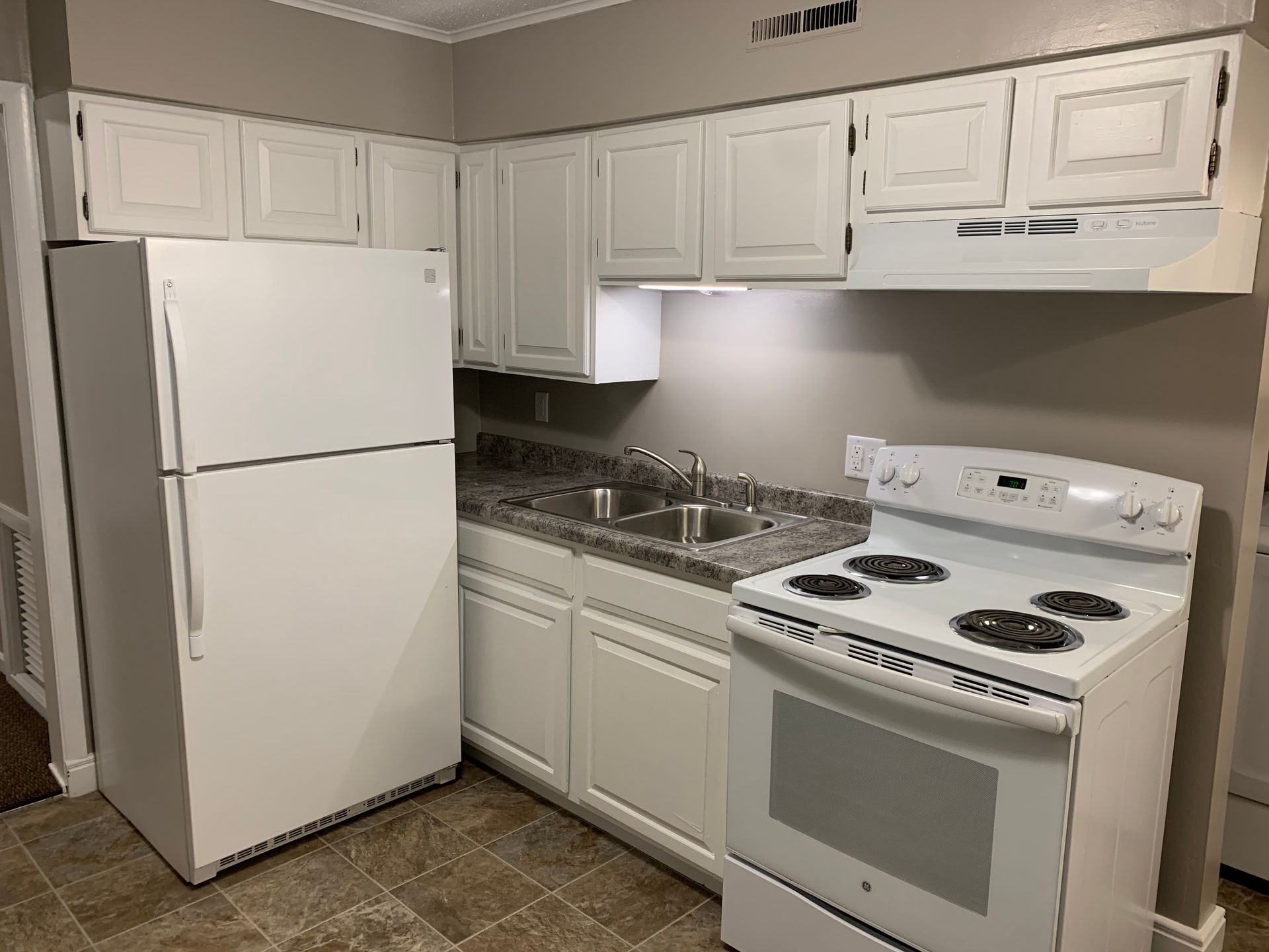 A kitchen with white cabinets , a refrigerator , stove and sink.