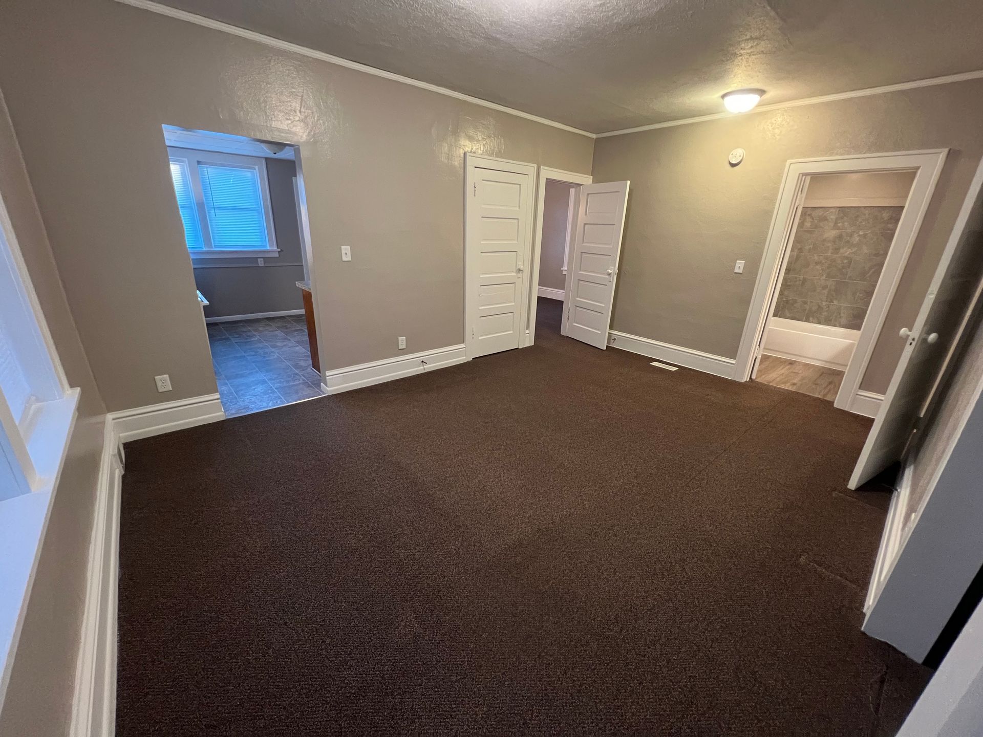 An empty living room with a brown carpet and gray walls.