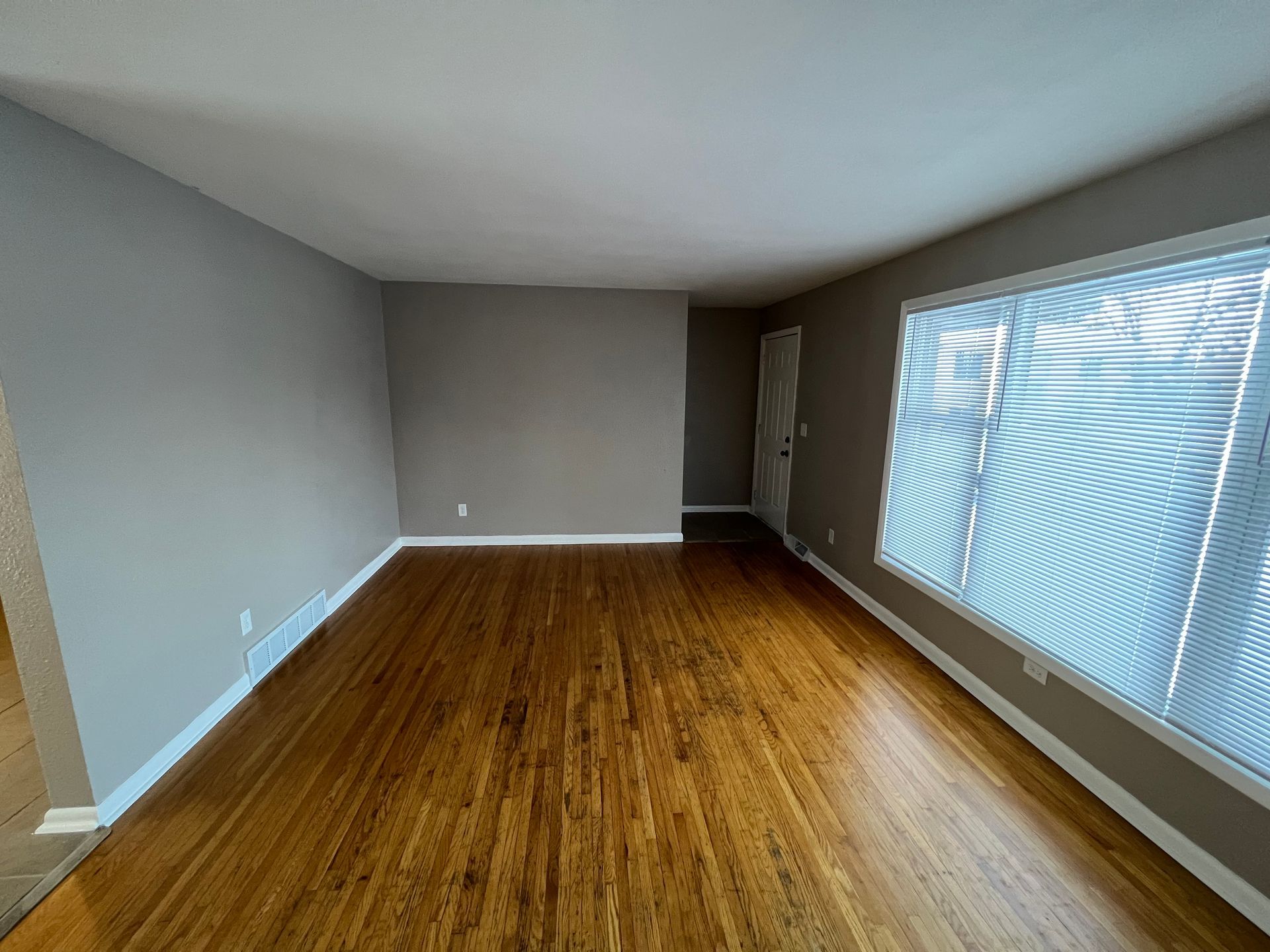 An empty living room with hardwood floors and gray walls.