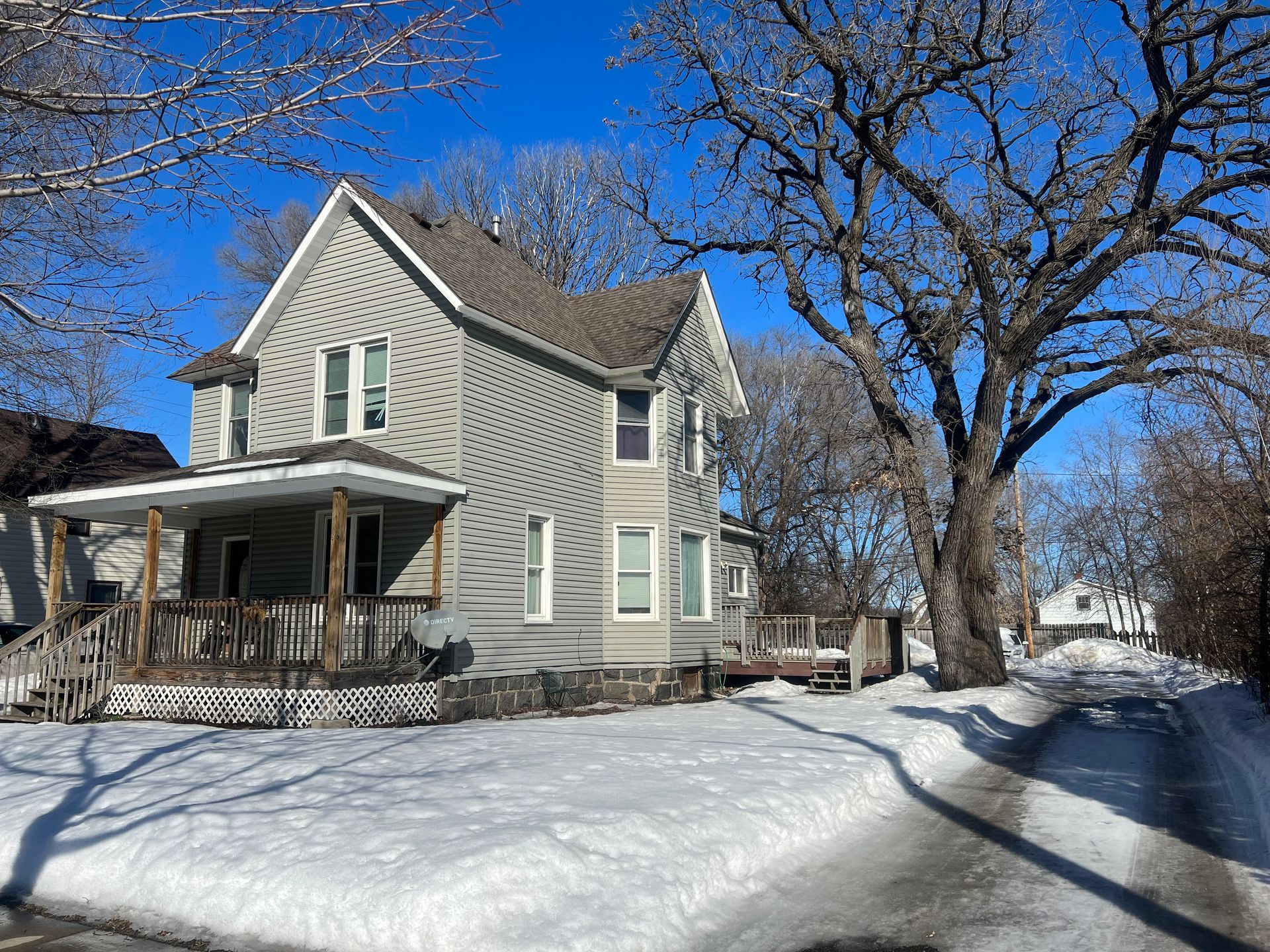 A house with a porch is surrounded by snow and trees.